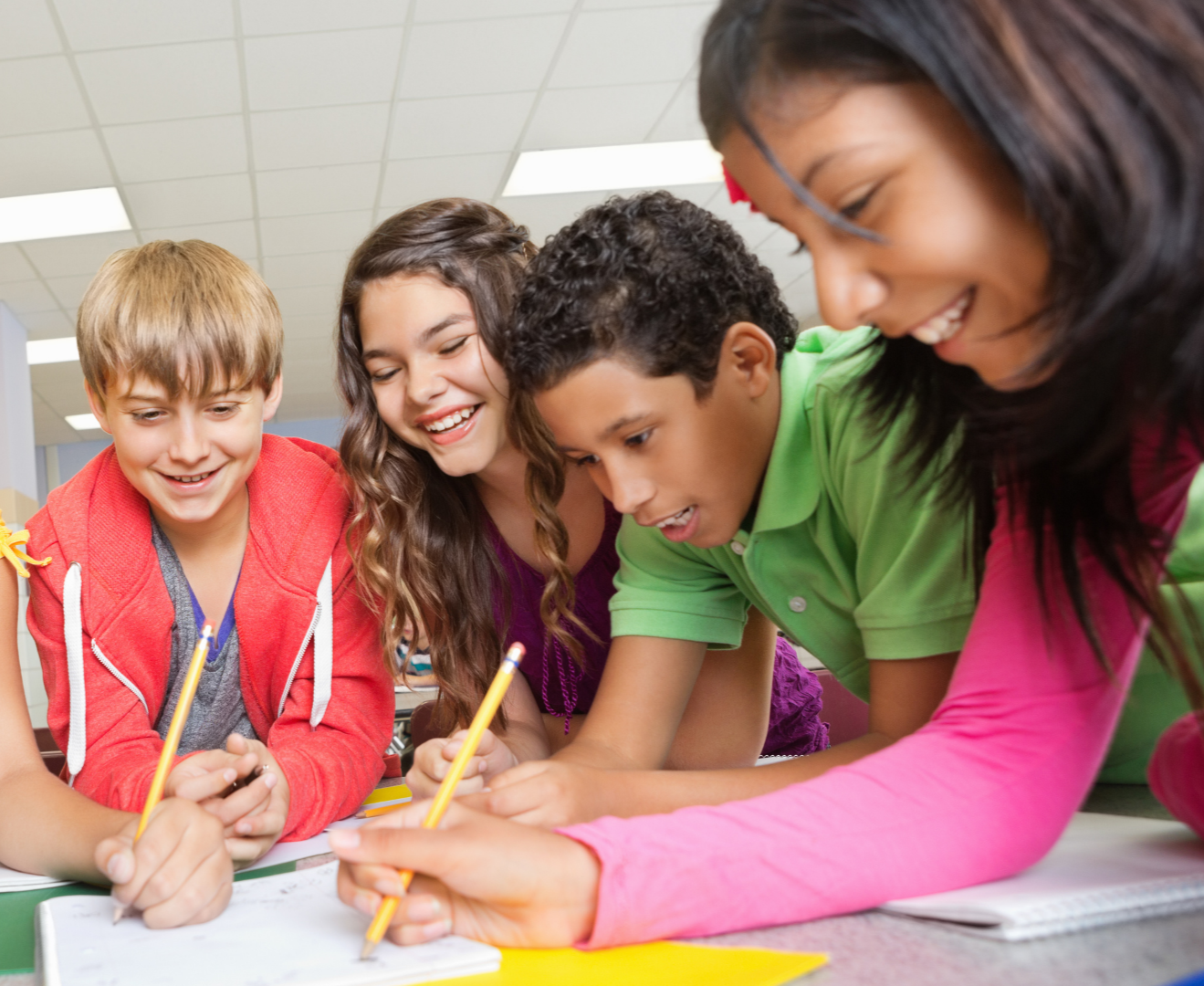 A group of diverse children gathered around a table, smiling and working together on a project with pencils.