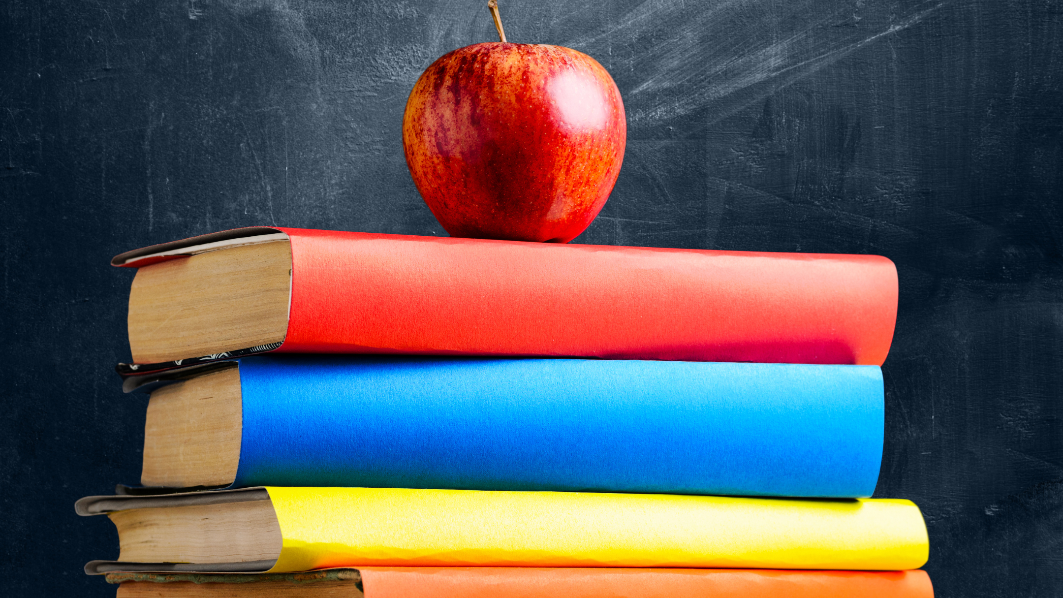 Stacked books with colored covers and a red apple on top, against a dark textured background.