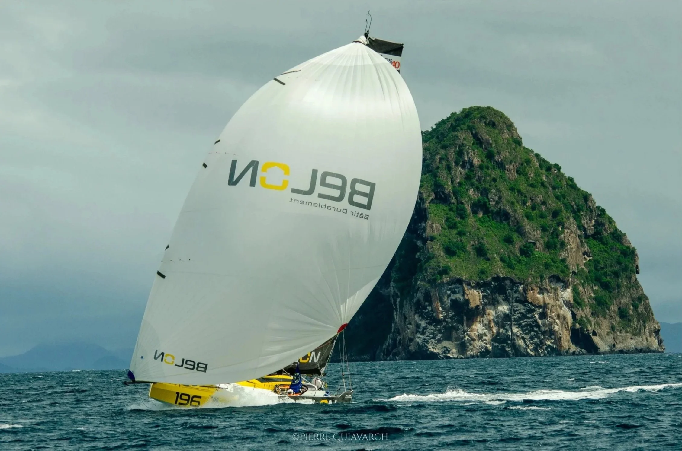 Voilier avec voilure déployée naviguant au large d'une île verdoyante