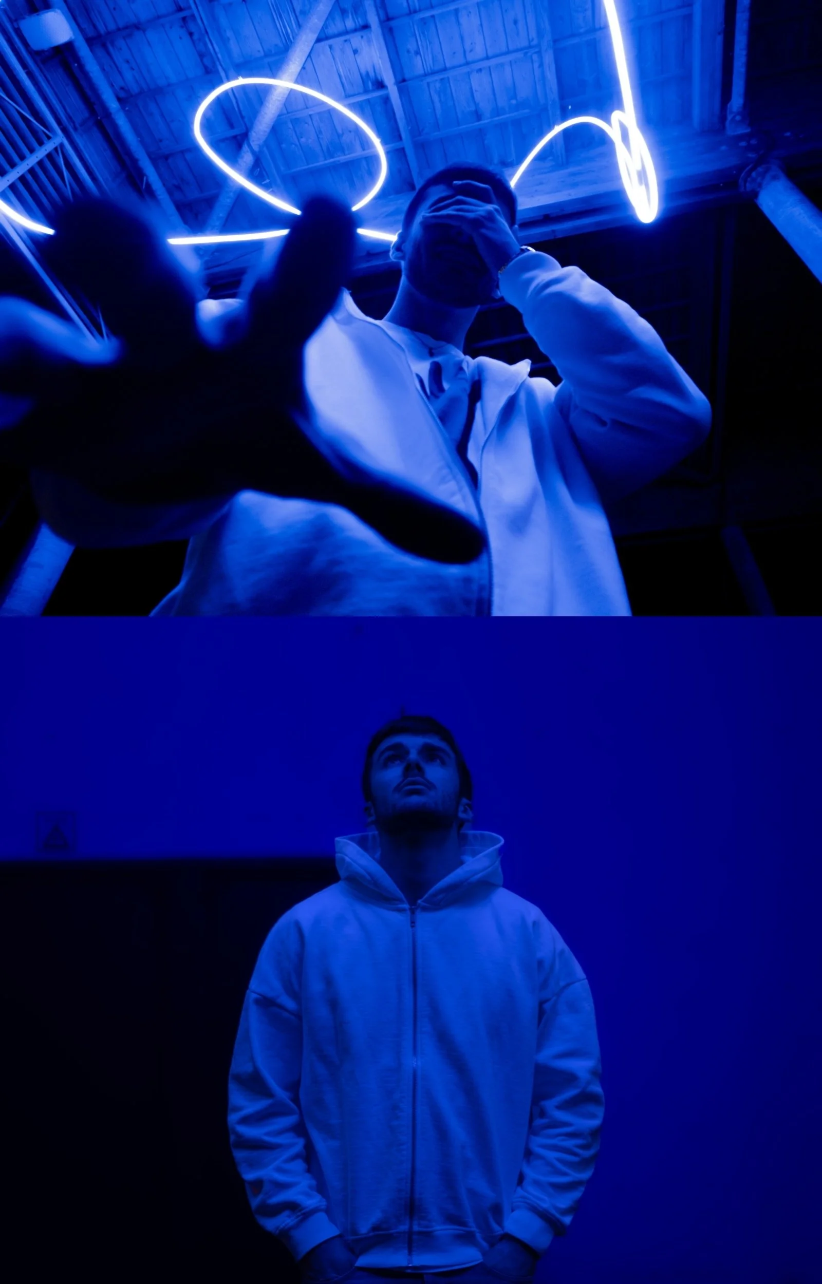 Deux jeunes hommes dans une pièce sombre, illuminés par des néons bleus et blancs. Le premier homme en premier plan porte un sweatshirt blanc et regarde vers le haut. Le deuxième homme en arrière-plan porte une veste blanche et regarde droit devant l