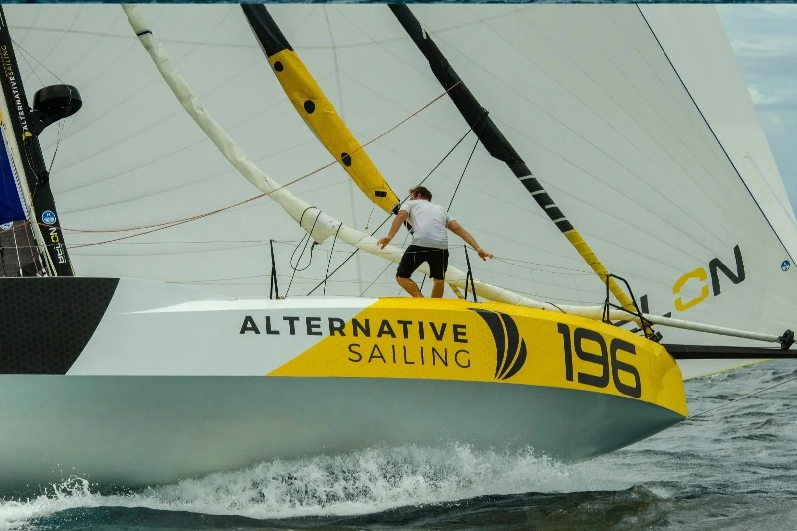 Voilier numérique jaune avec le texte 'ALTERNATIVE SAILING' et le numéro '196', un homme à bord en train de naviguer sur la mer.
