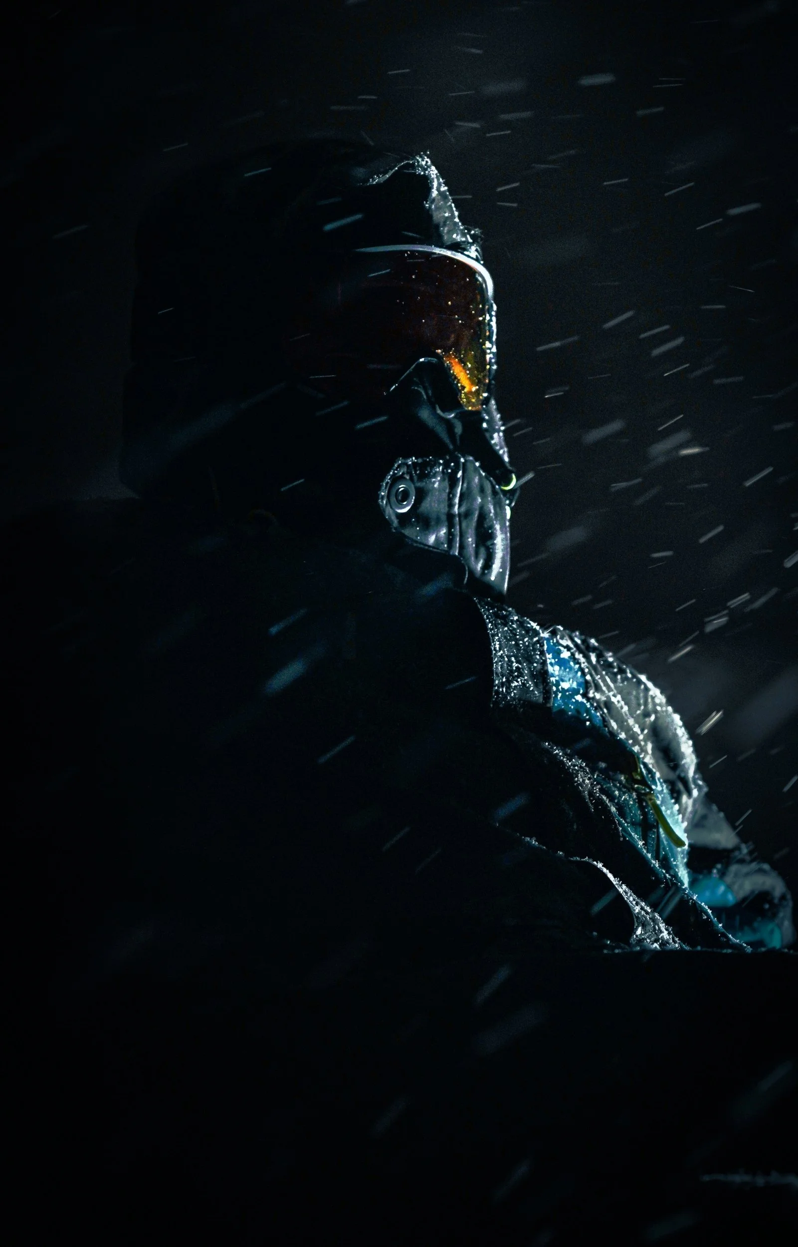 Une personne portant un casque de ski et des lunettes de ski dans une ambiance sombre, avec des flocons de neige visibles.