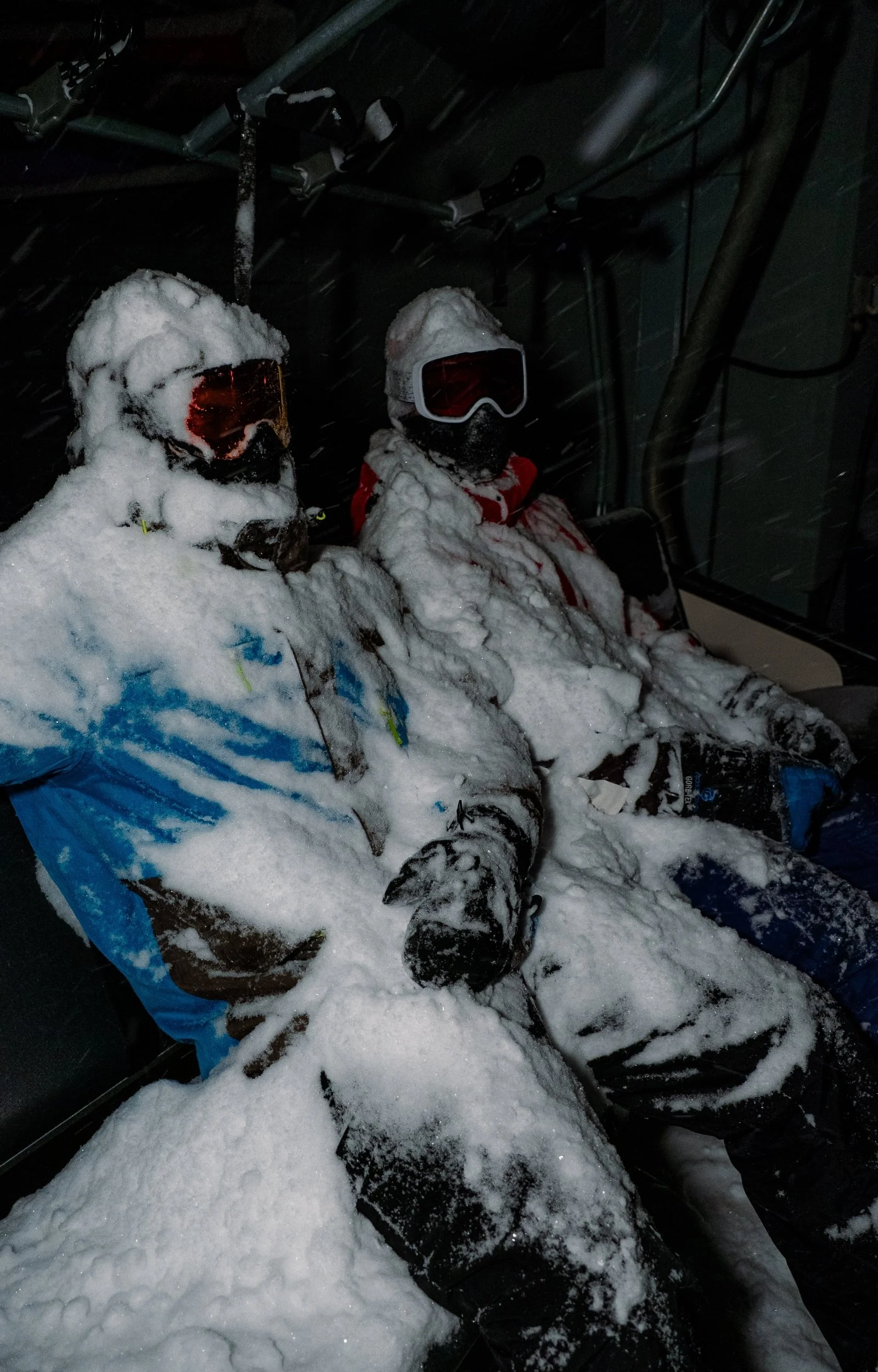 Deux enfants en équipement de ski dans une pièce sombre, recouverts de neige.