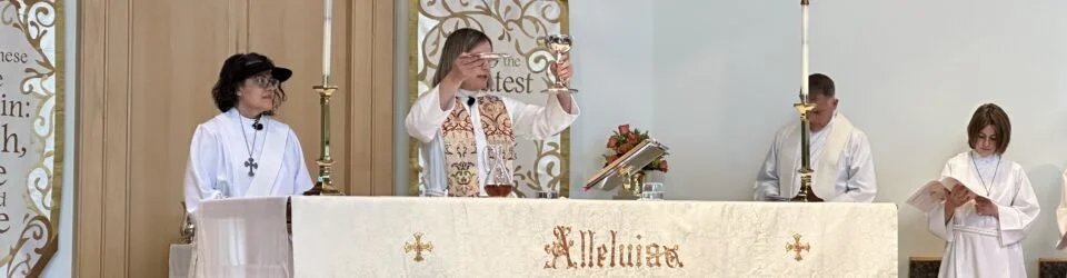 A religious ceremony with four clergy members standing behind an altar, including a priest in the center holding a chalice, others reading or standing with hands ready, in a church setting with gold accents and lit candles.