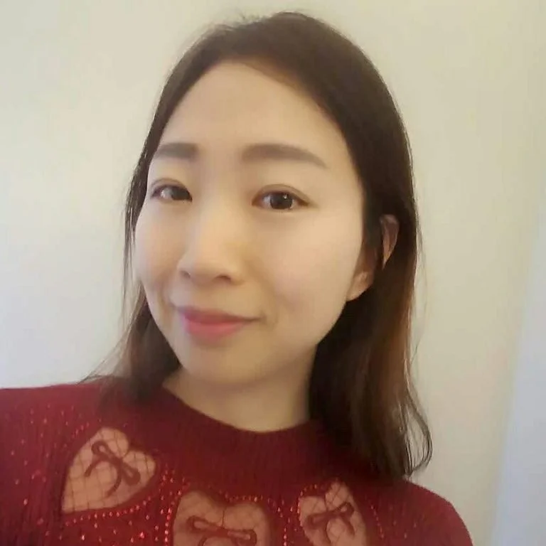 A woman with shoulder-length dark hair smiling in front of a plain background, wearing a red sweater with heart-shaped cutouts.