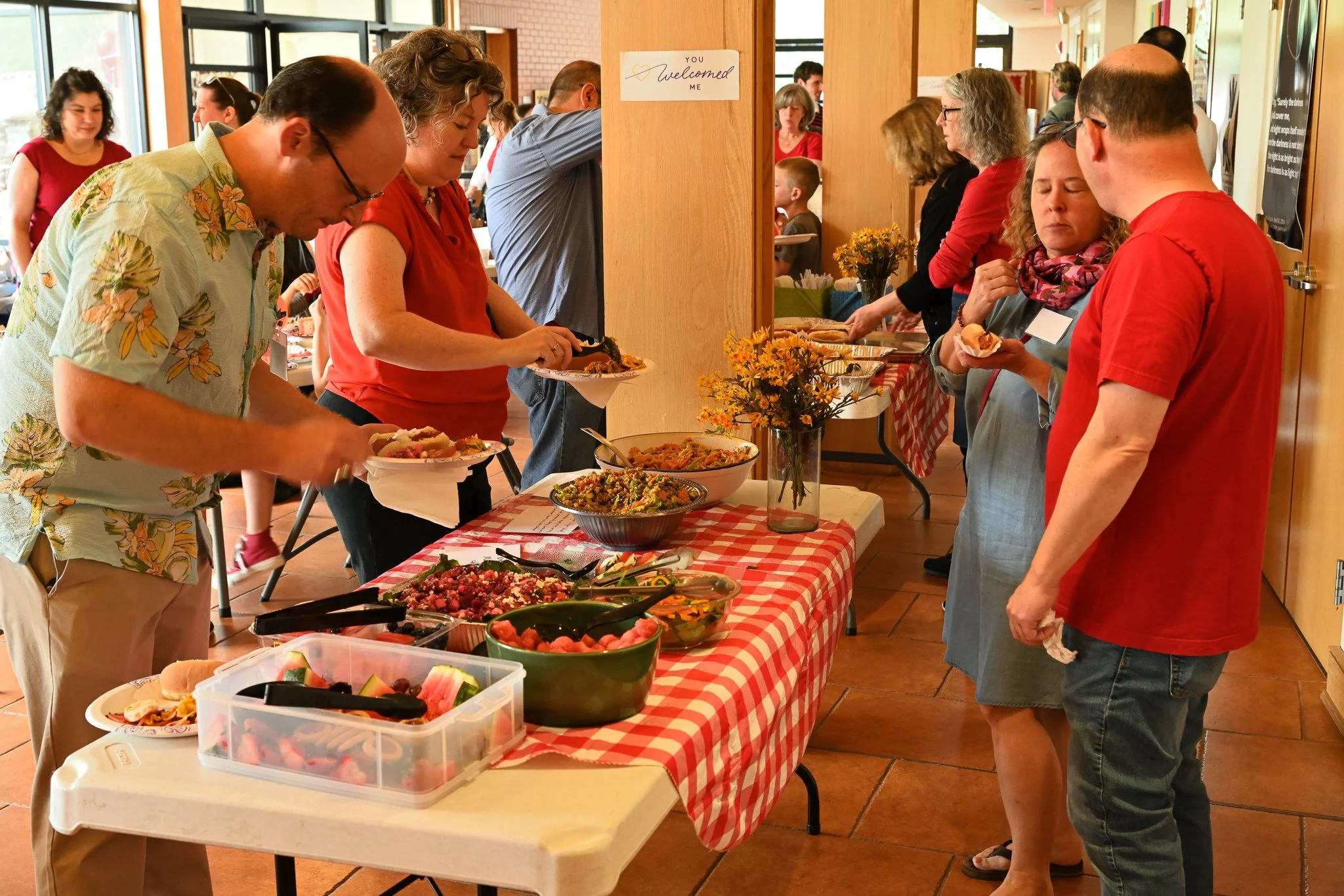 People serving themselves food at a buffet table with various dishes, inside a well-lit room with wooden decor.