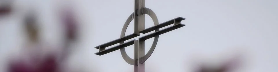 Close-up of a metallic cross-shaped weather vane against a cloudy sky