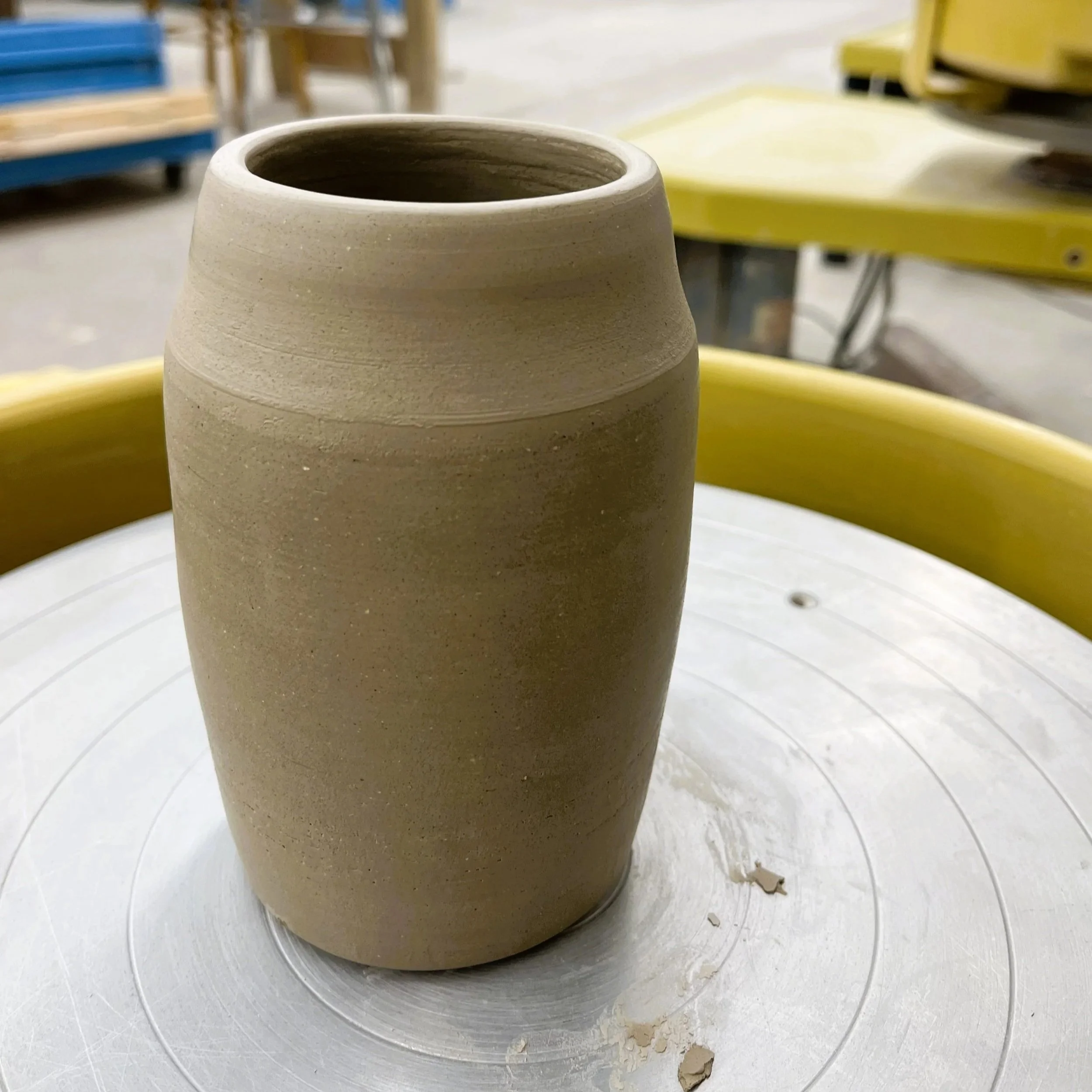 A ceramic pot or vase under construction on a pottery wheel with clay residue and small pieces of clay around it.