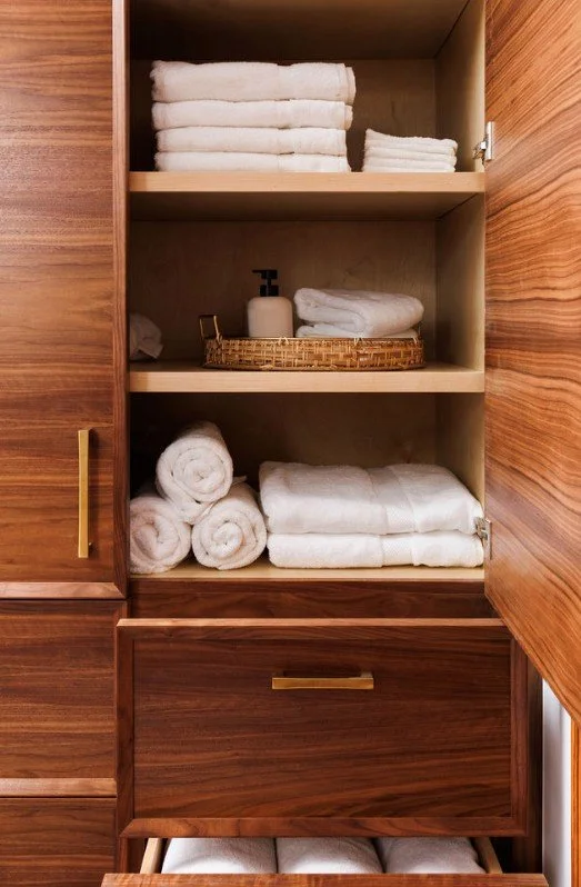 Open wooden cabinet with shelves containing neatly folded white towels and a soap dispenser.