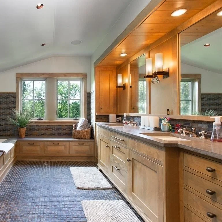 Bathroom with wooden cabinets, a large mirror, a sink with toiletries, and a vanity seating area by the window with a potted plant, brick accents, and mosaic tile flooring.
