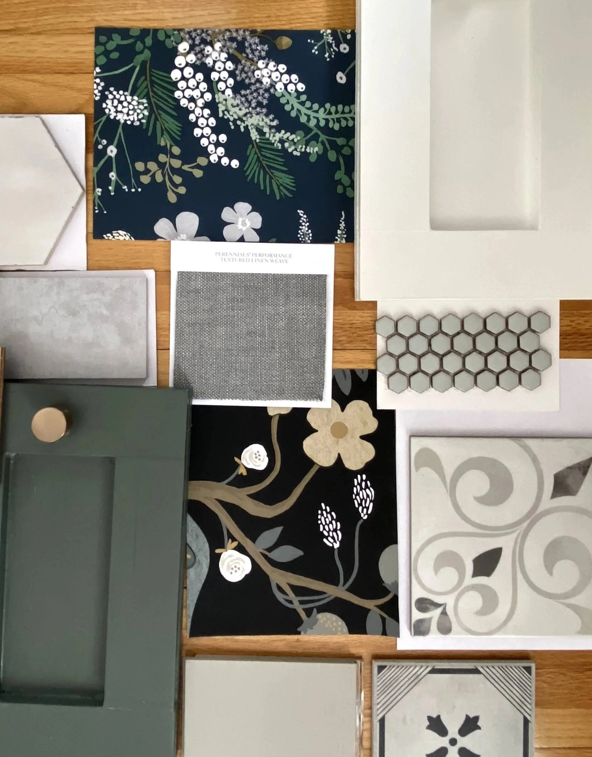 A display of tile samples and fabric swatches on a wooden surface, including floral and geometric patterns in various colors.
