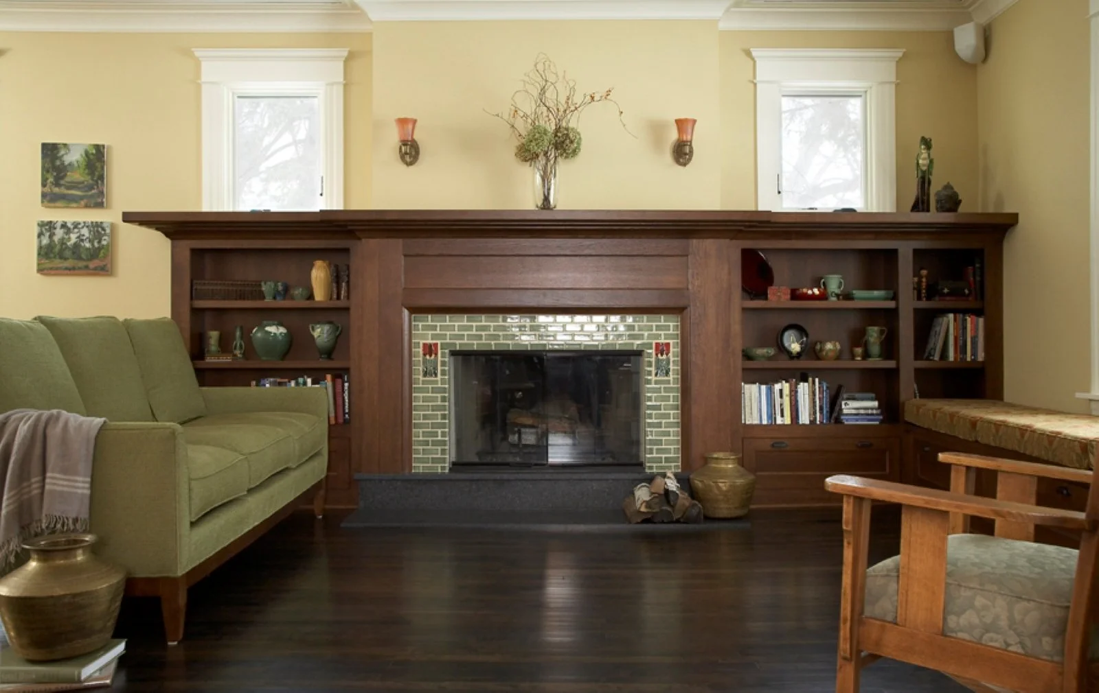 Living room with a fireplace, wooden mantle, built-in shelves, green sofa, and armchair, windows, and decorative items.