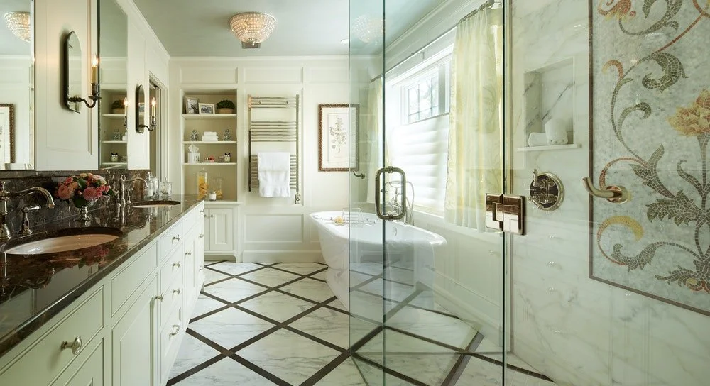 A luxurious bathroom with dual sinks, a shower with glass doors, a bathtub near a window, and elegant decor.
