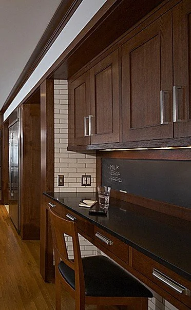 Wooden cabinetry above a black countertop in a kitchen or bar area with a chalkboard and a glass of water.