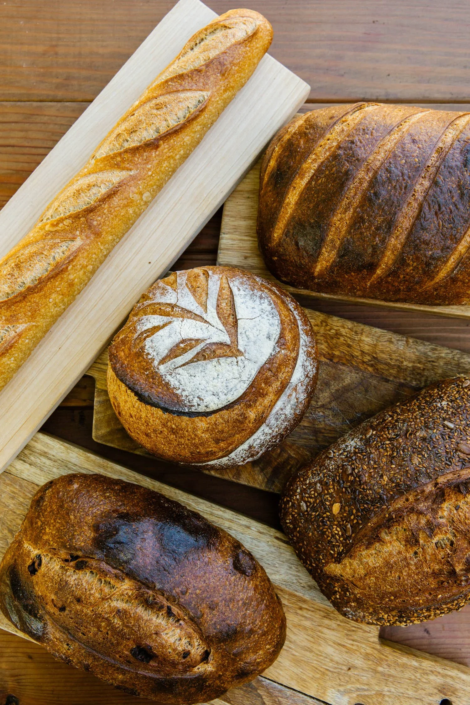 Assortment of delicious Ojai Rôtie sourdough breads — boules, baguette, and scored loaves on a wooden board