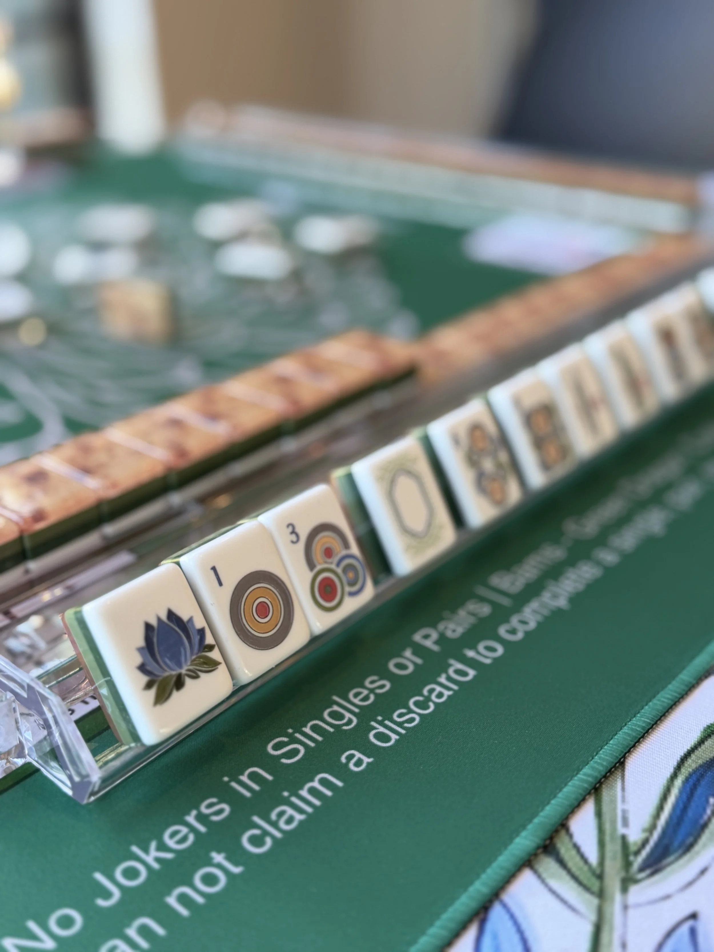 Close-up of Mahjong tiles arranged in a row on a green game mat, with other Mahjong tiles visible in the background.