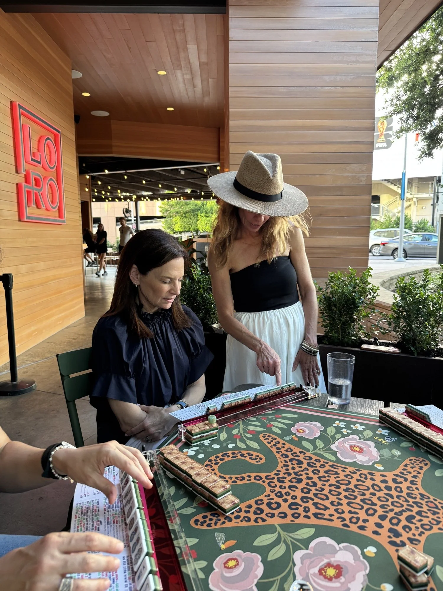 Laurie teaching mahjong in a hat on the patio at Loro in Austin