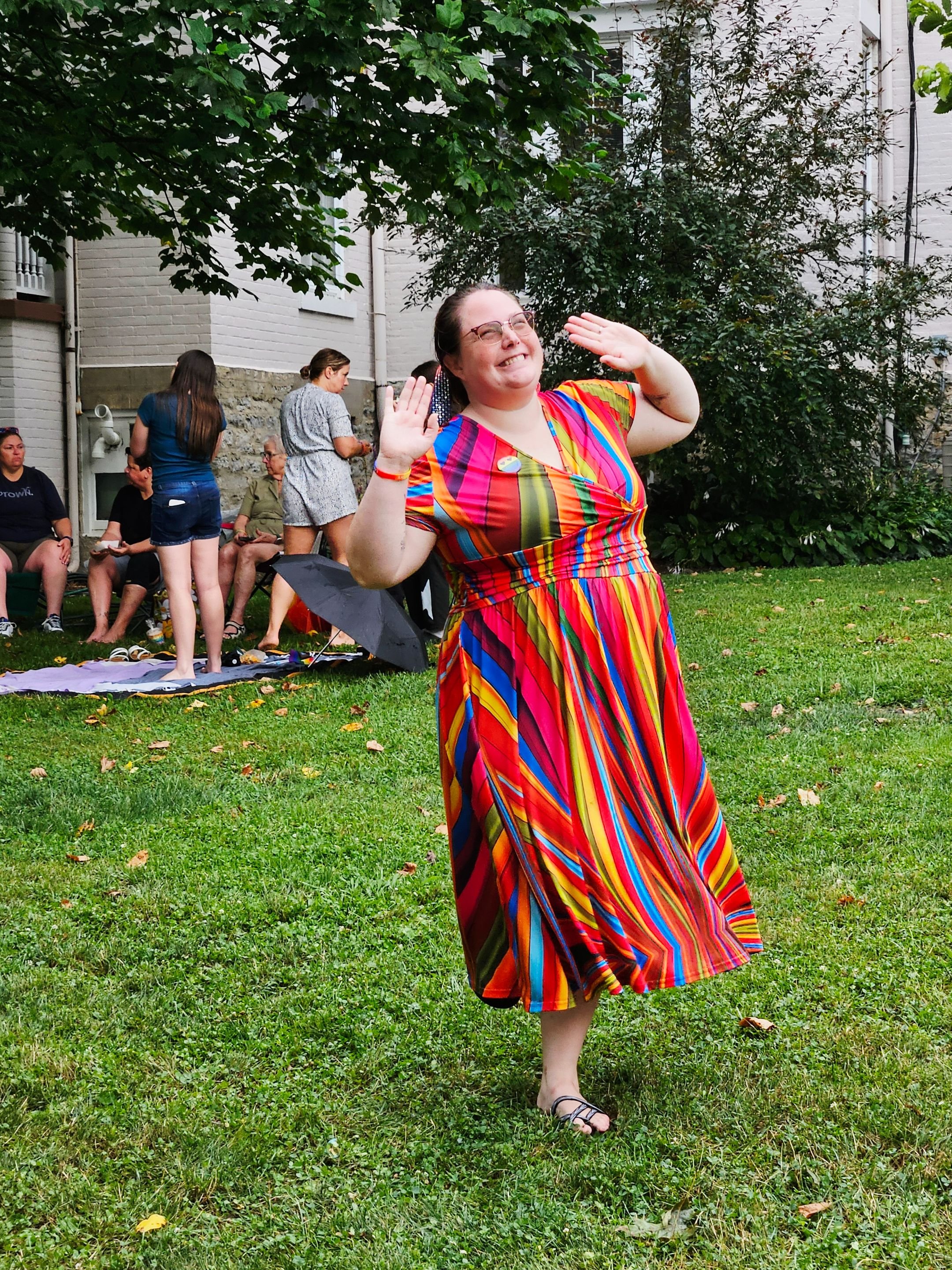 A woman dances in the rain to music at the 2025 Glendale CommUNITY Concert. She is wearing a long rainbow colored dress.
