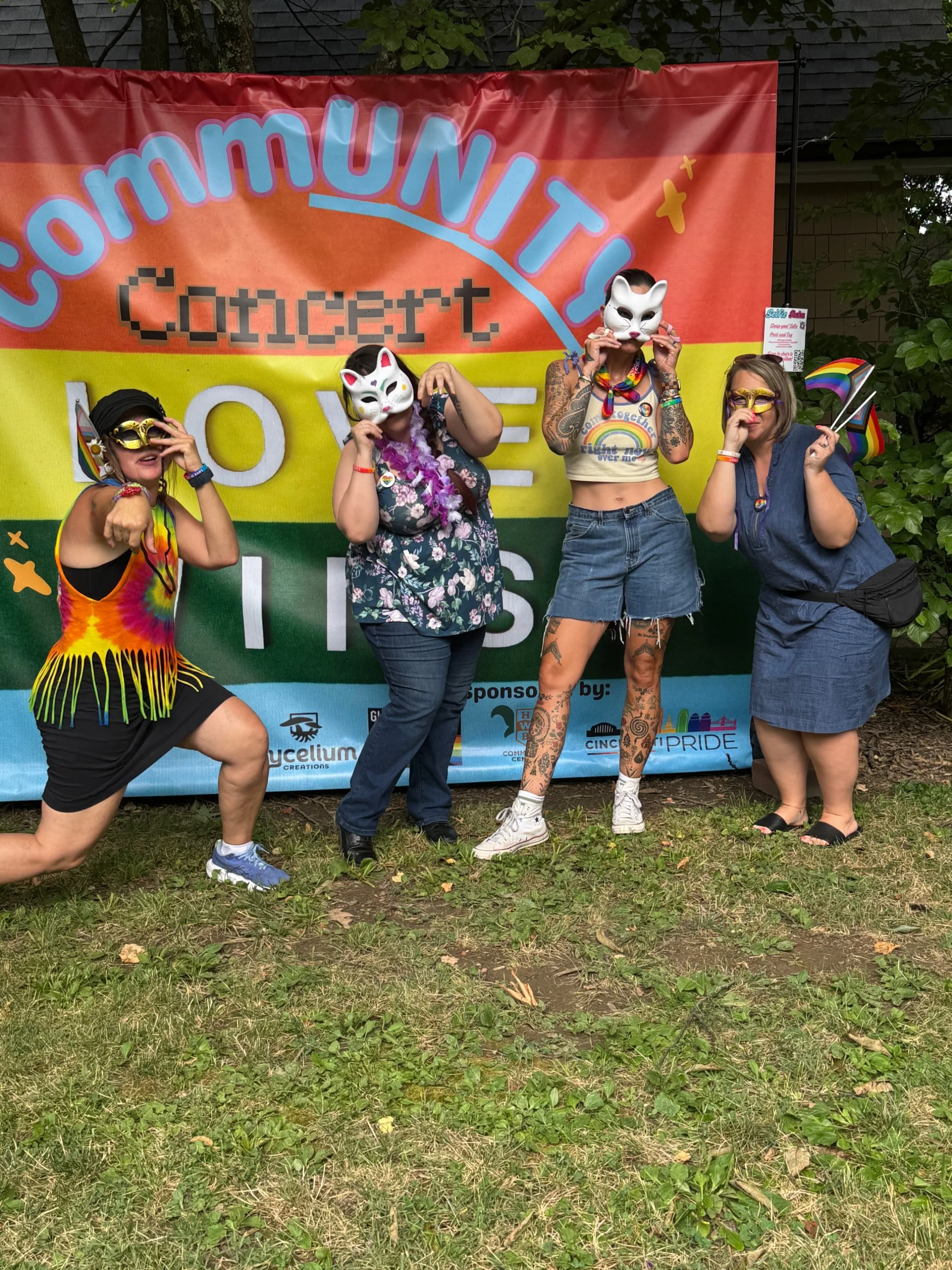 four women posing in front of the a banner that says "CommUNITY Concert, Love Wins."  The banner is designed with a rainbow flag.