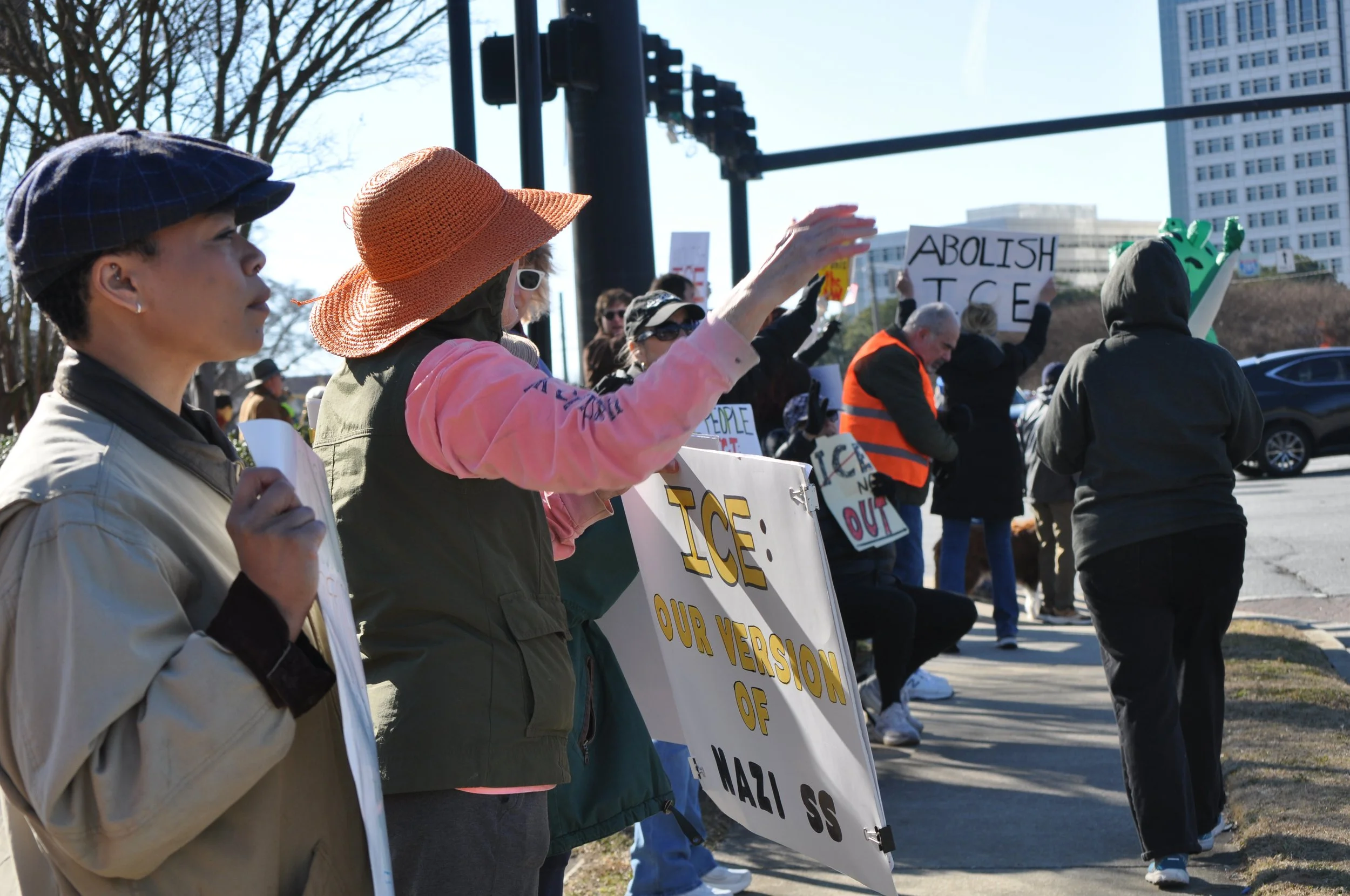 People participating in a protest holding signs and banners with messages about abolishing ICE and opposing fascism, standing on a sidewalk in an urban area.