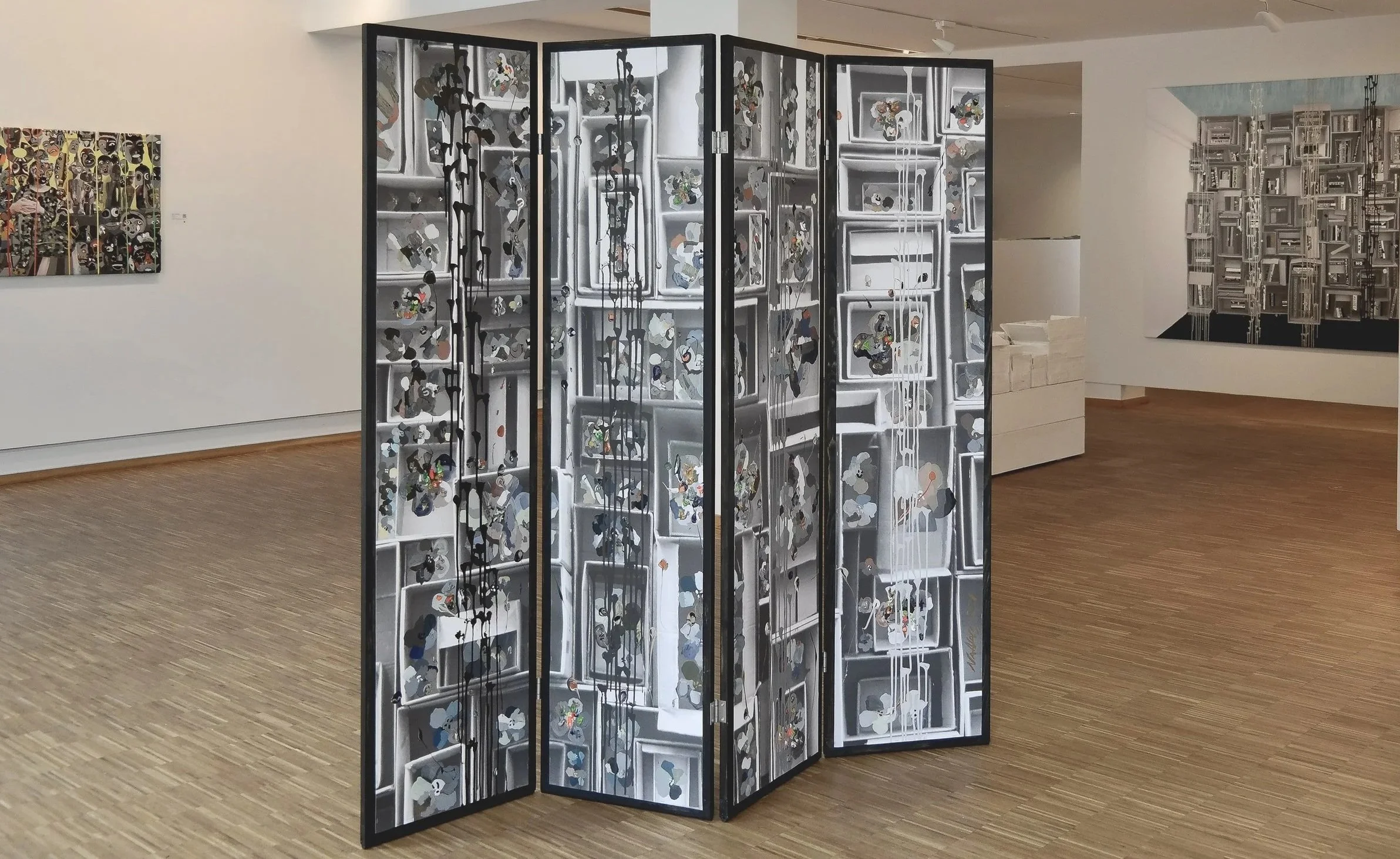 A folding art display panel in an art gallery, featuring a black dividers with an abstract black, white, and gray design that resembles a collage of various images.