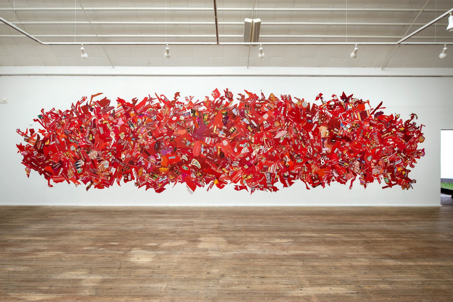 A large wall mural made of assorted red candy wrappers and packaging, arranged in an abstract, wavy pattern.