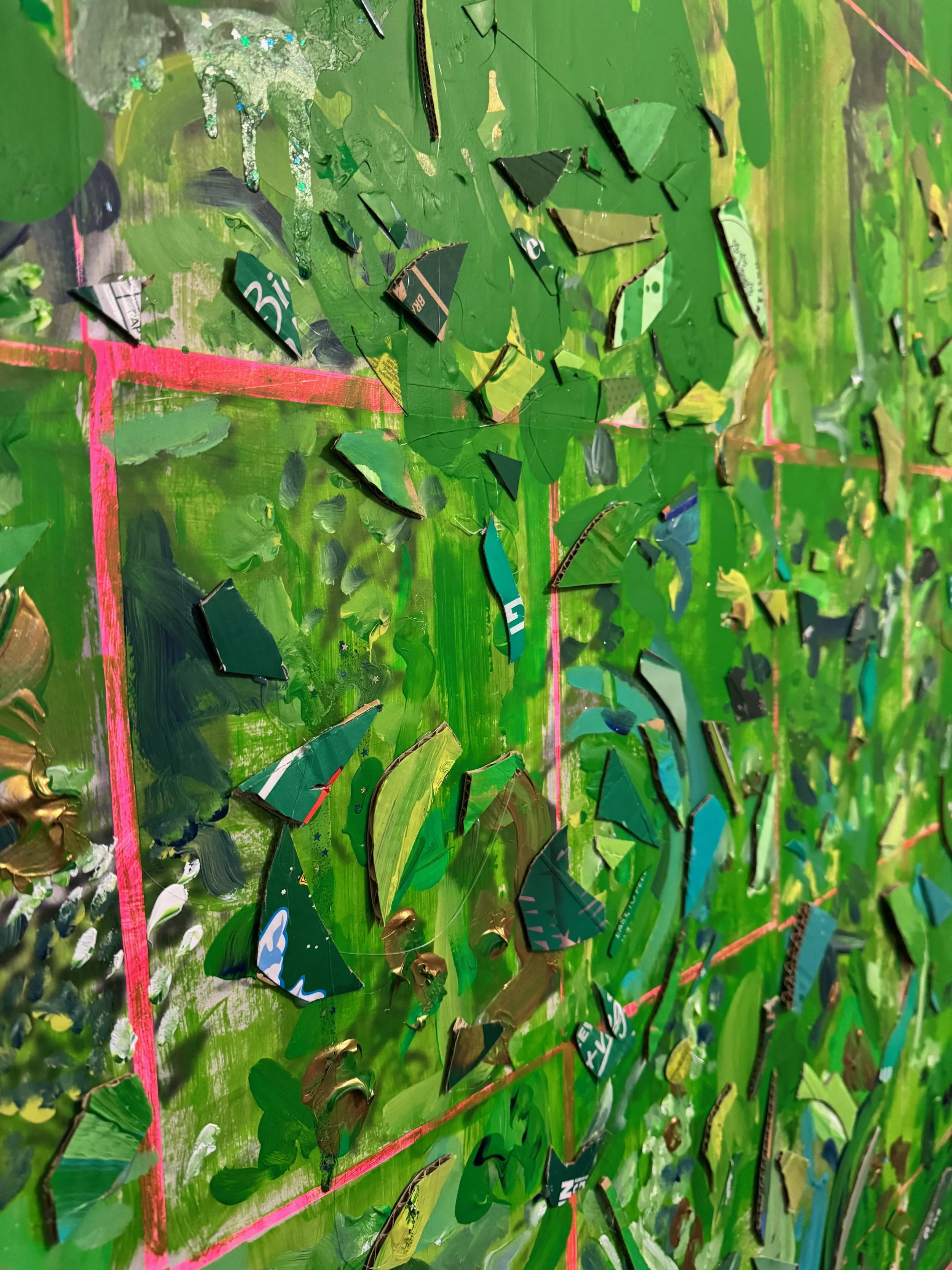 Close-up of a creative art piece featuring a green background with painted layers and scattered torn pieces of magazine or newspaper paper, some with text and patterns, on a grid marked with pink tape.