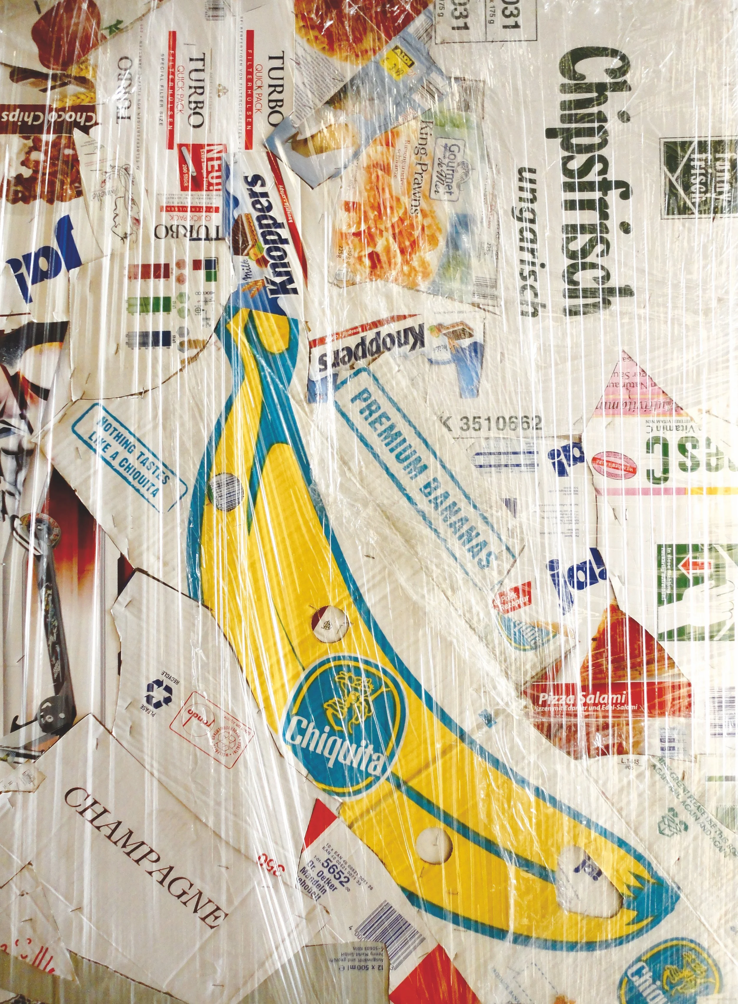 A bundle of various cardboard food packages and product wrappers wrapped in clear plastic, including a Chiquita banana sticker, a Kraft cheese product, and other snack and grocery items.