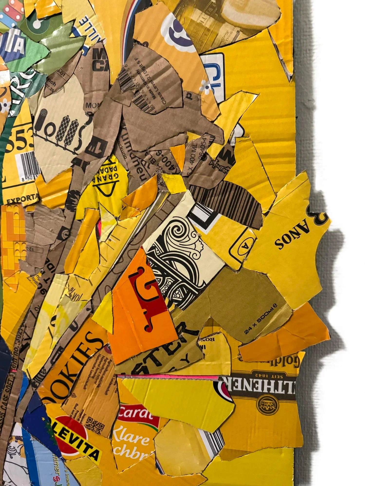 Collage of torn and crumpled pieces of colorful food packaging, mostly in yellow, orange, and brown, arranged on a flat surface.