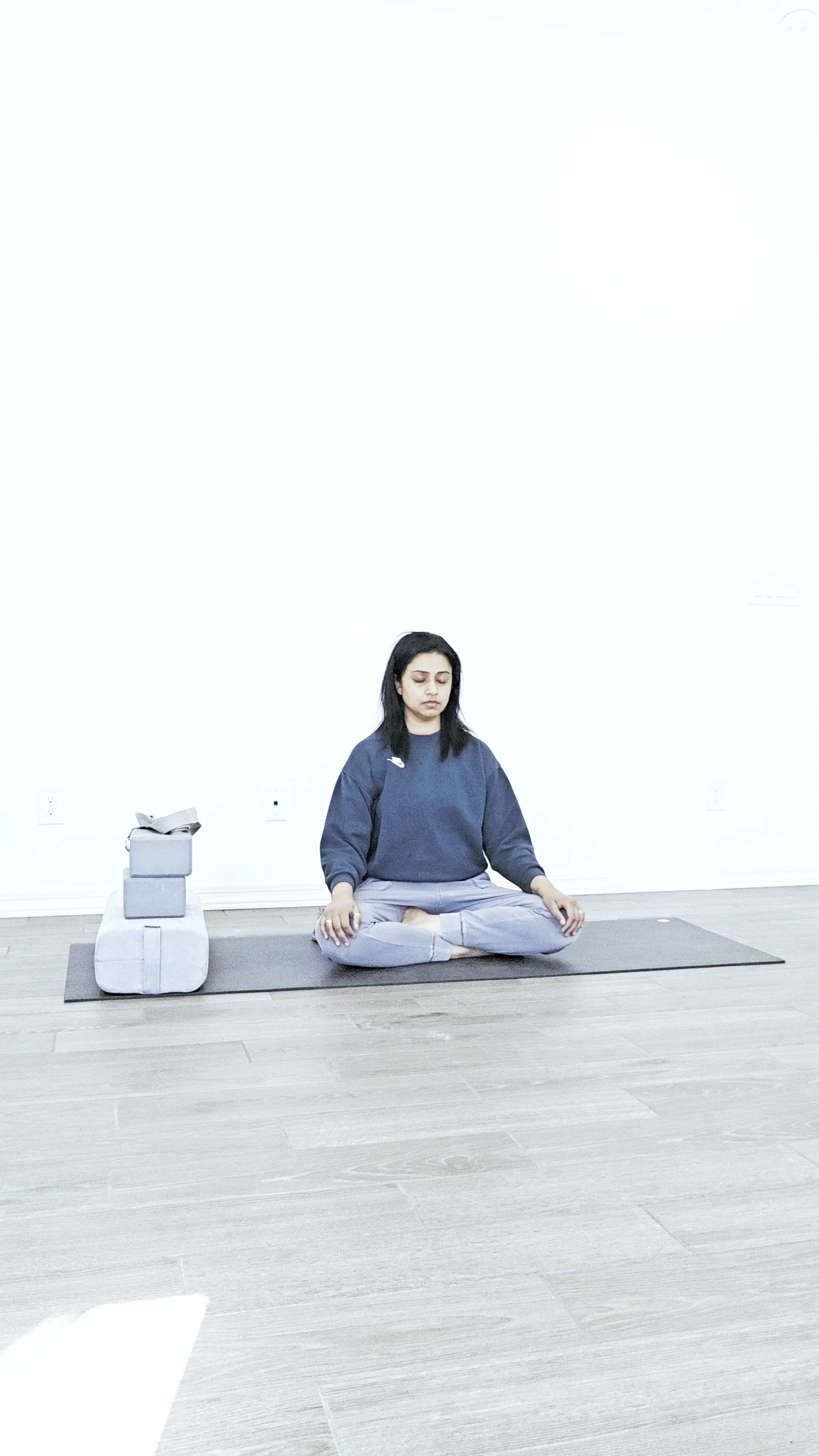 Person seated in meditation beside yoga props on a yoga mat