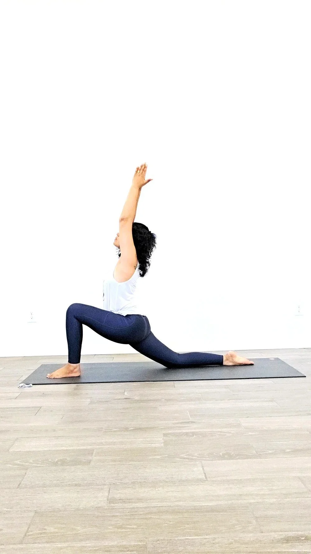 Person practicing a low lunge with arms reaching overhead on a yoga mat.