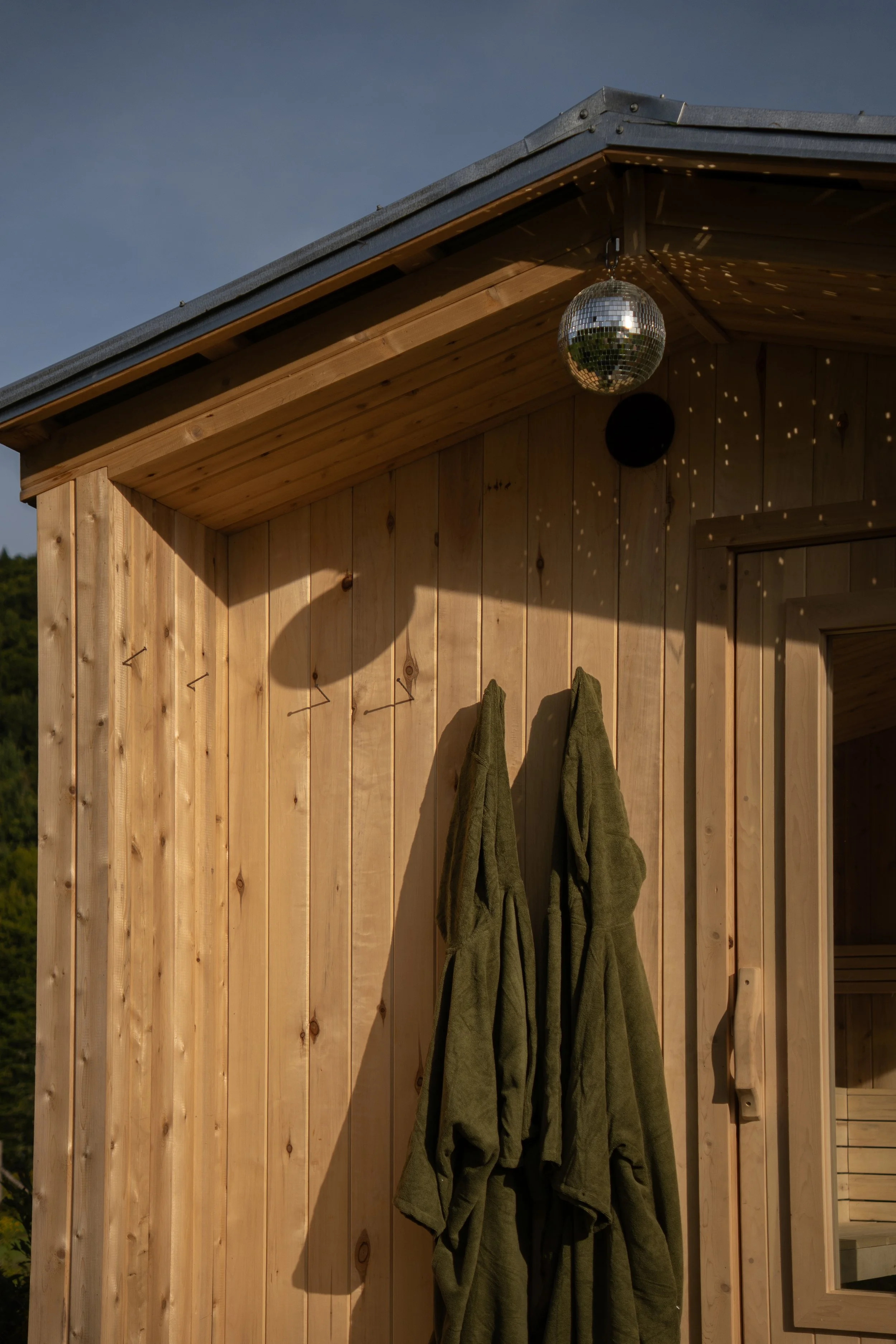 Un mur en bois avec deux vestes vertes suspendues et un miroir disco suspendu au plafond, projetant des reflets lumineux.