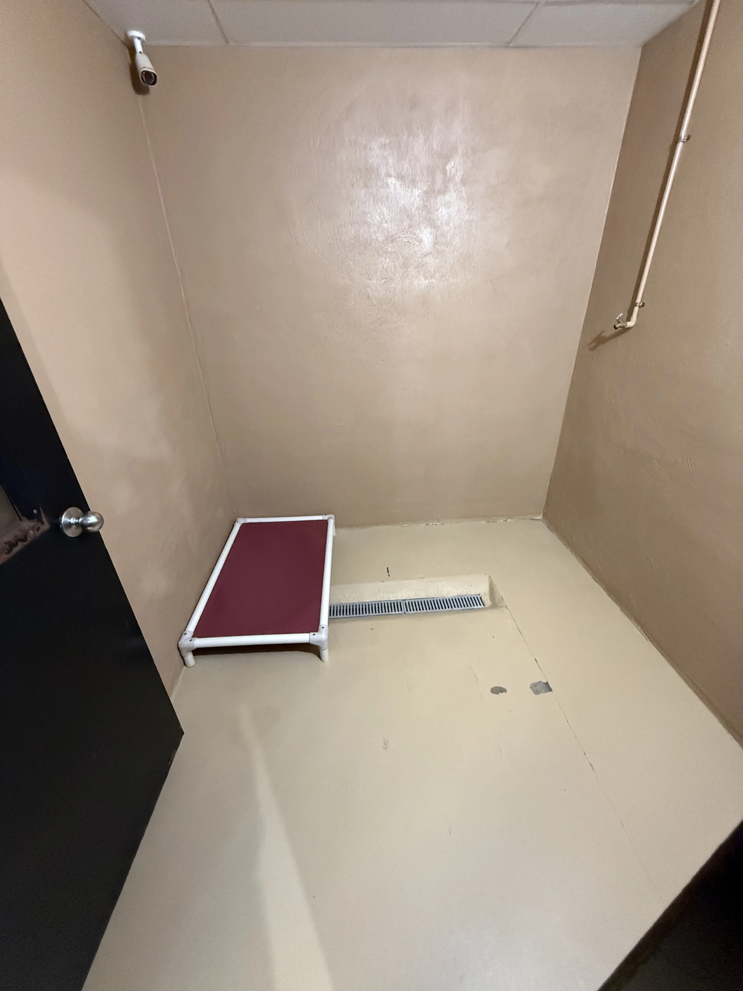 Empty beige room with a security camera in the upper left corner, a red pet step, and a floor vent.