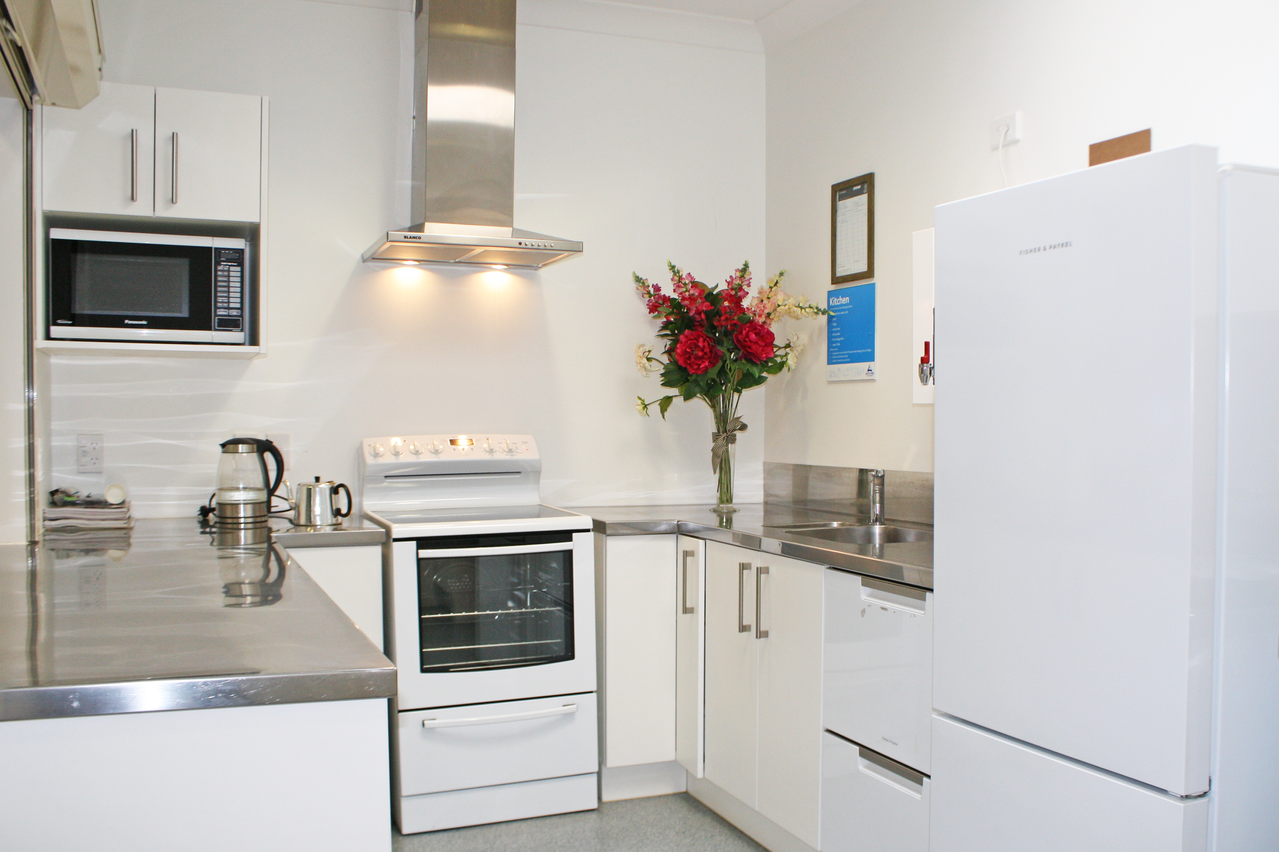 Kitchen with white cabinets, stainless steel countertop, white stove, microwave, refrigerator, and a vase of red and pink flowers on the counter.