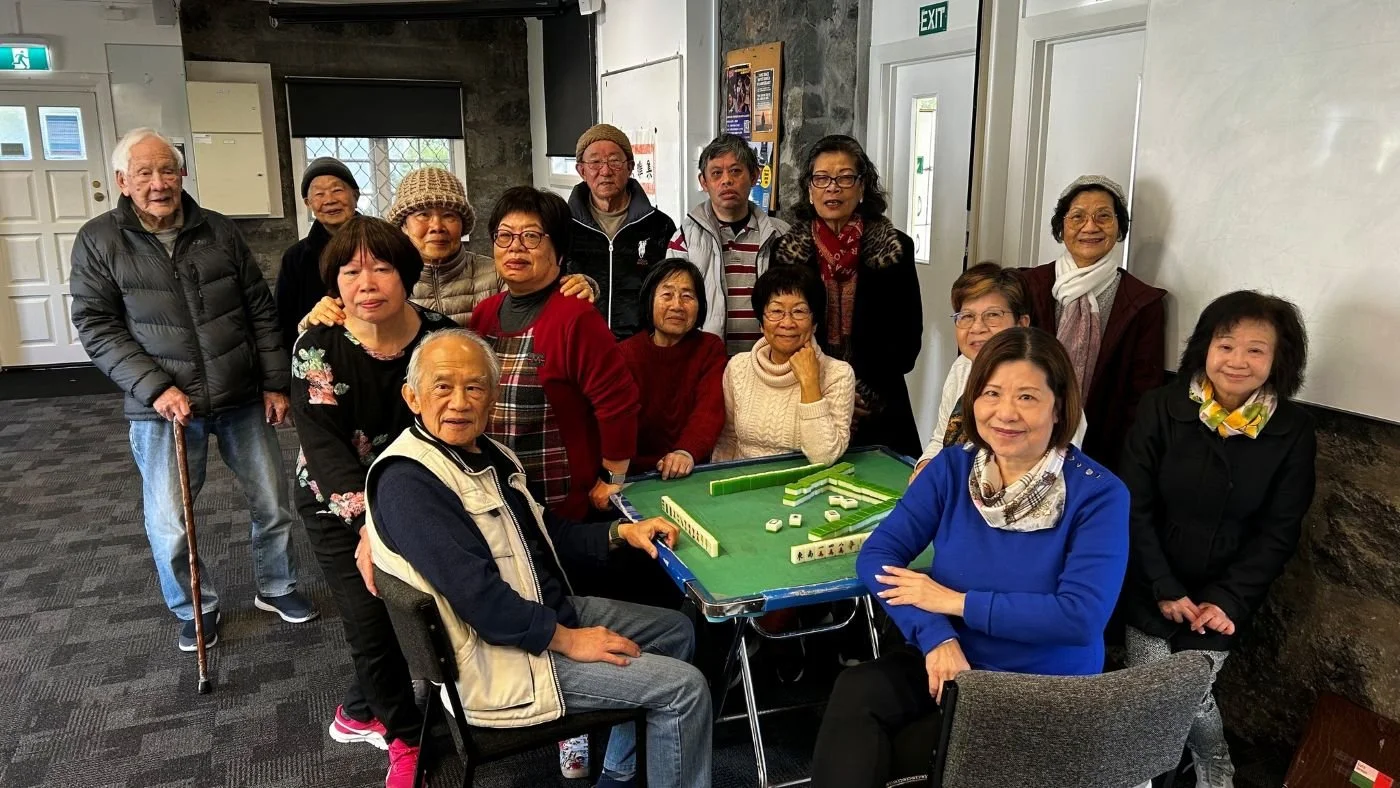 The Epsom Joyful Cantonese Group sitting around a game of Mah Jong, smiling