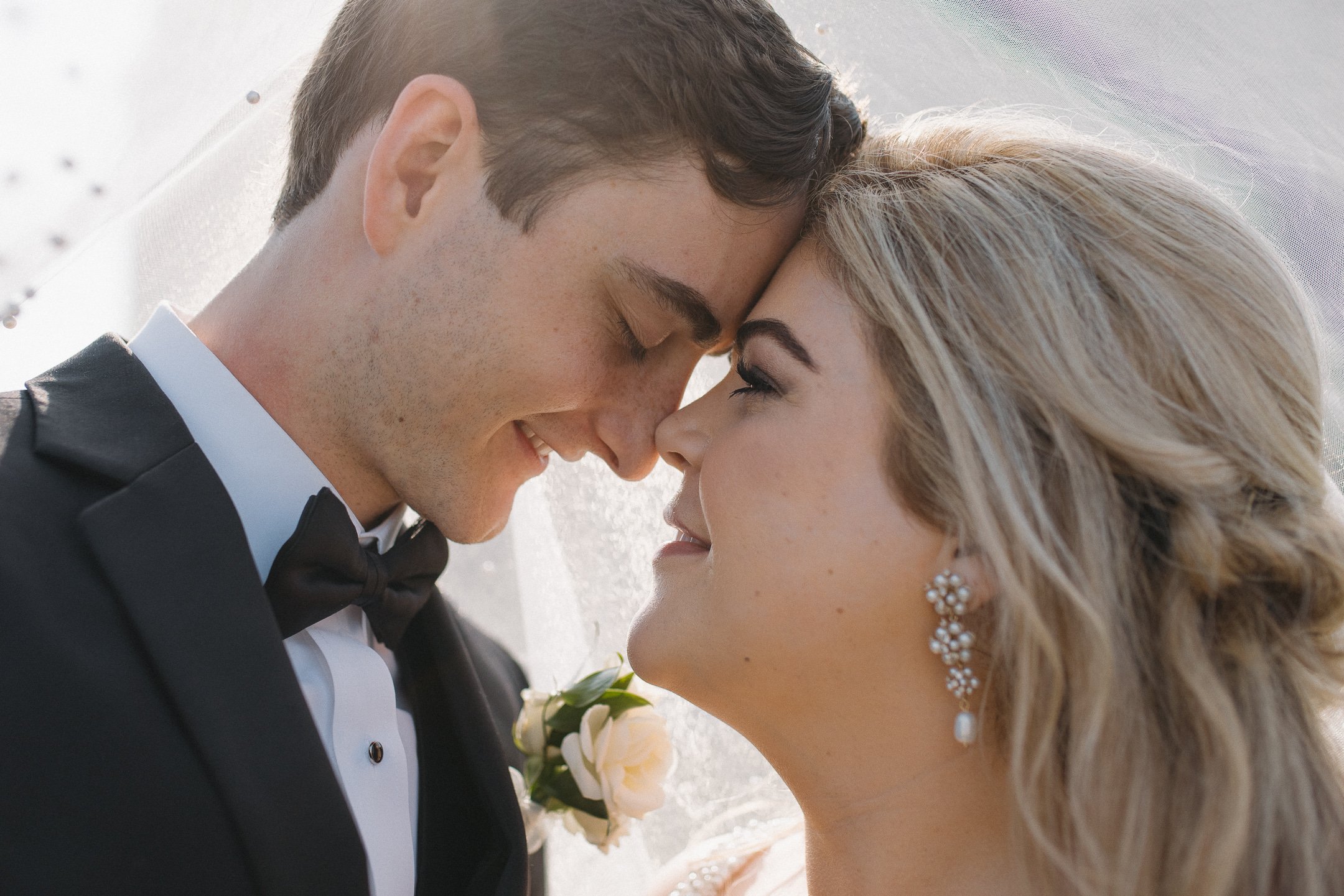 Close-up of a bride and groom with touching foreheads and smiling faces, dressed in wedding attire, on their wedding day.