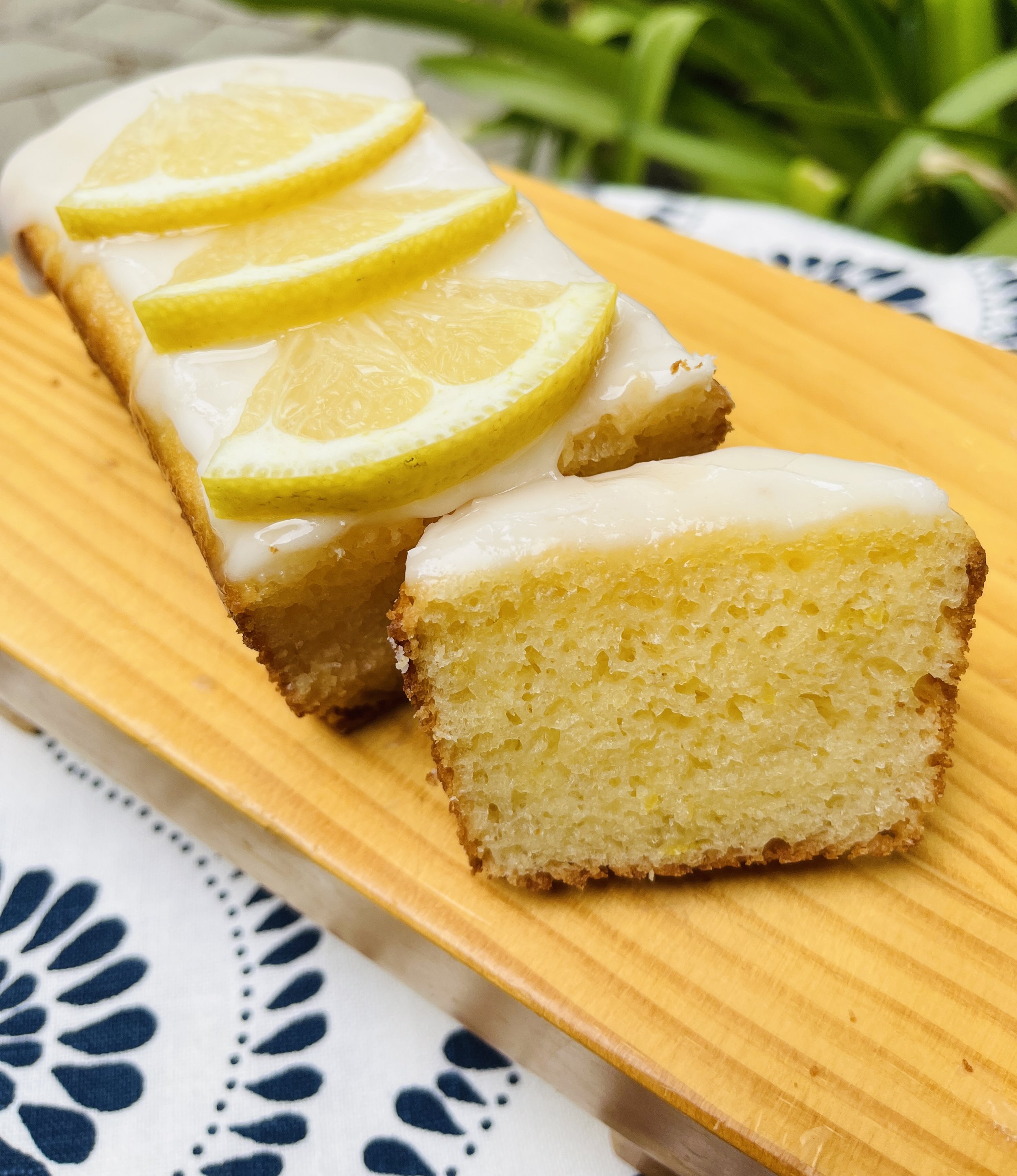 Lemon pound cake with lemon slices on top and white icing, placed on a wooden serving board.