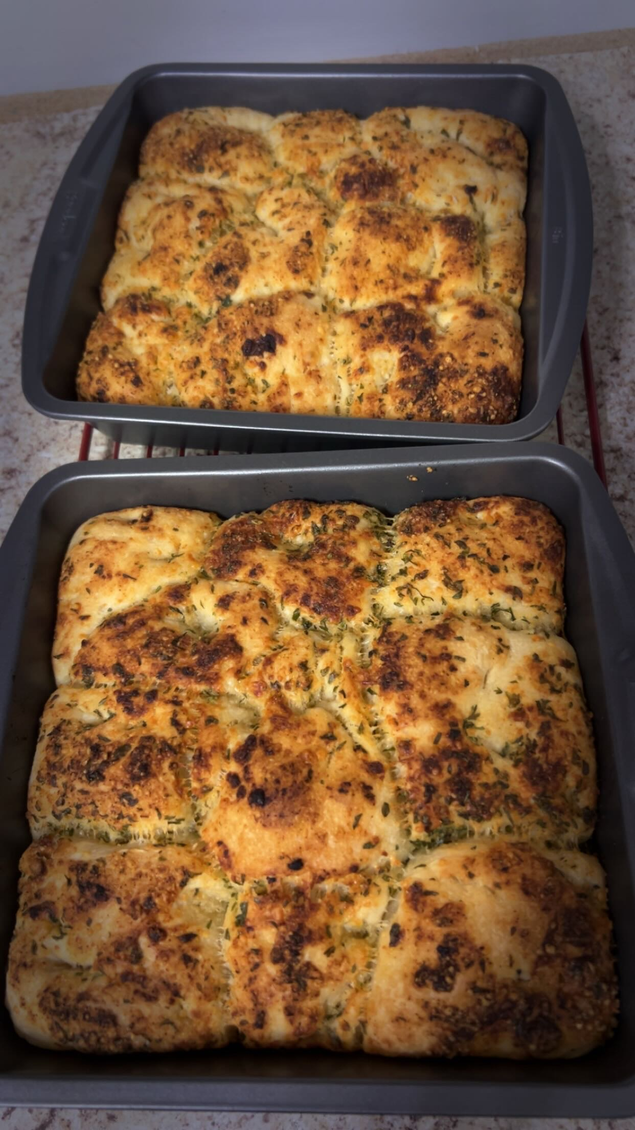 Two baking trays filled with cooked garlic bread topped with herbs and melted cheese