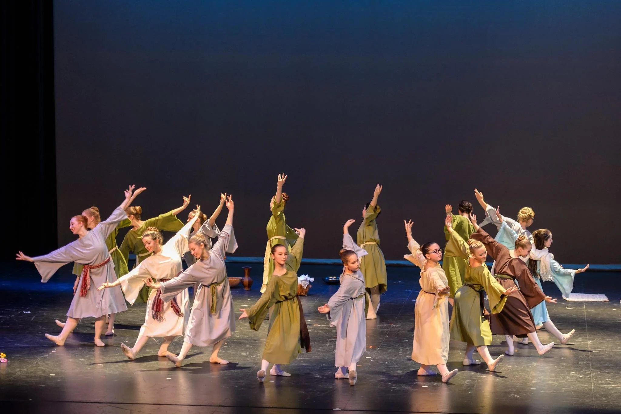 A group of performers in traditional costumes performing a dance on stage with a dark background and stage lights.