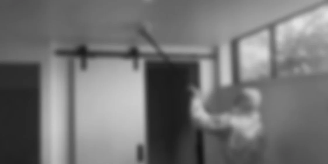 Two children playing in a room with large windows, a sliding door, and a door leading outside. One child is reaching out to the other, near a pull-up bar.