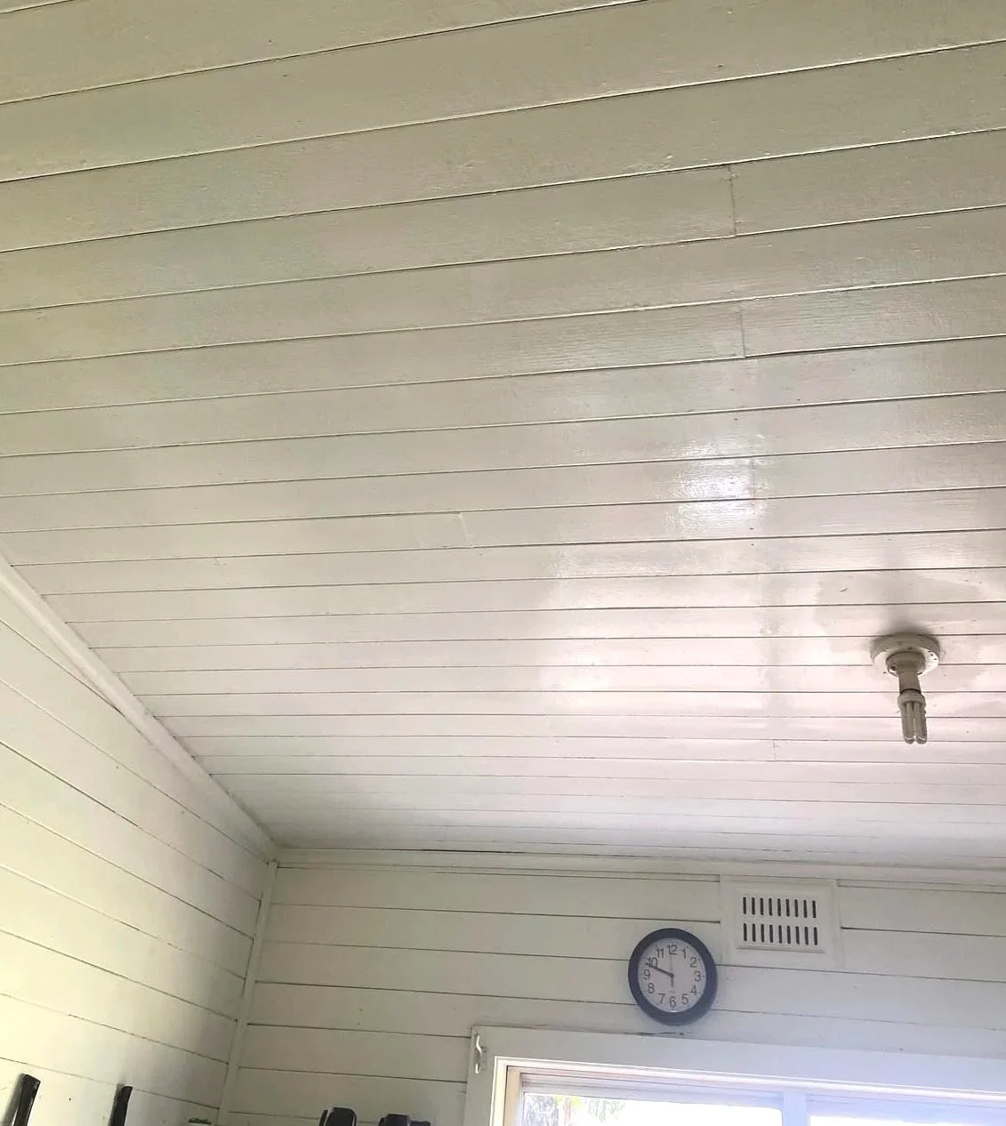 Interior ceiling with white wood paneling, a wall clock showing 9:47, and a light bulb fixture.