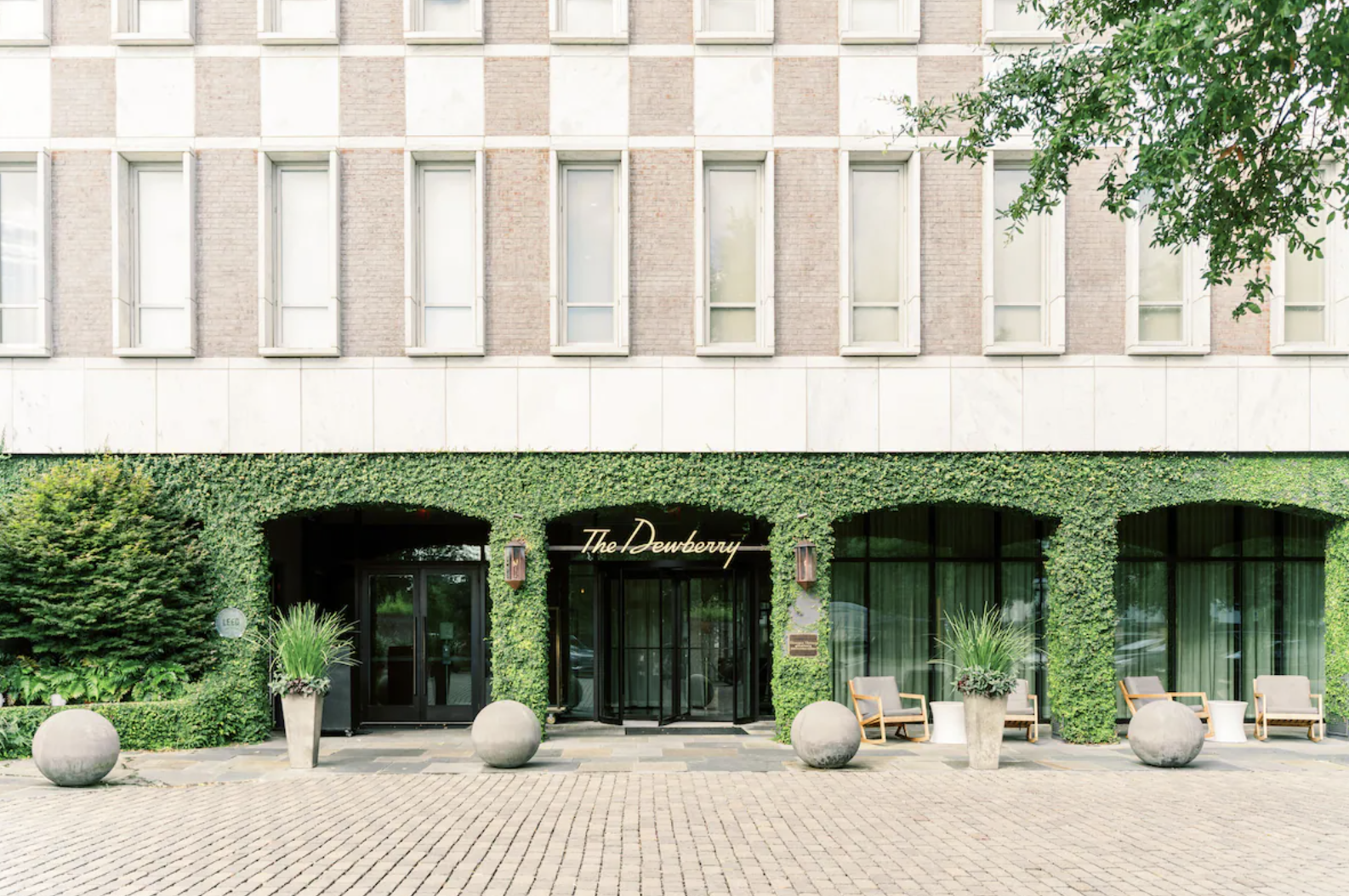 Exterior shot of a building with a green ivy facade, glass doors, and large windows, with seating and decorative planters outside.