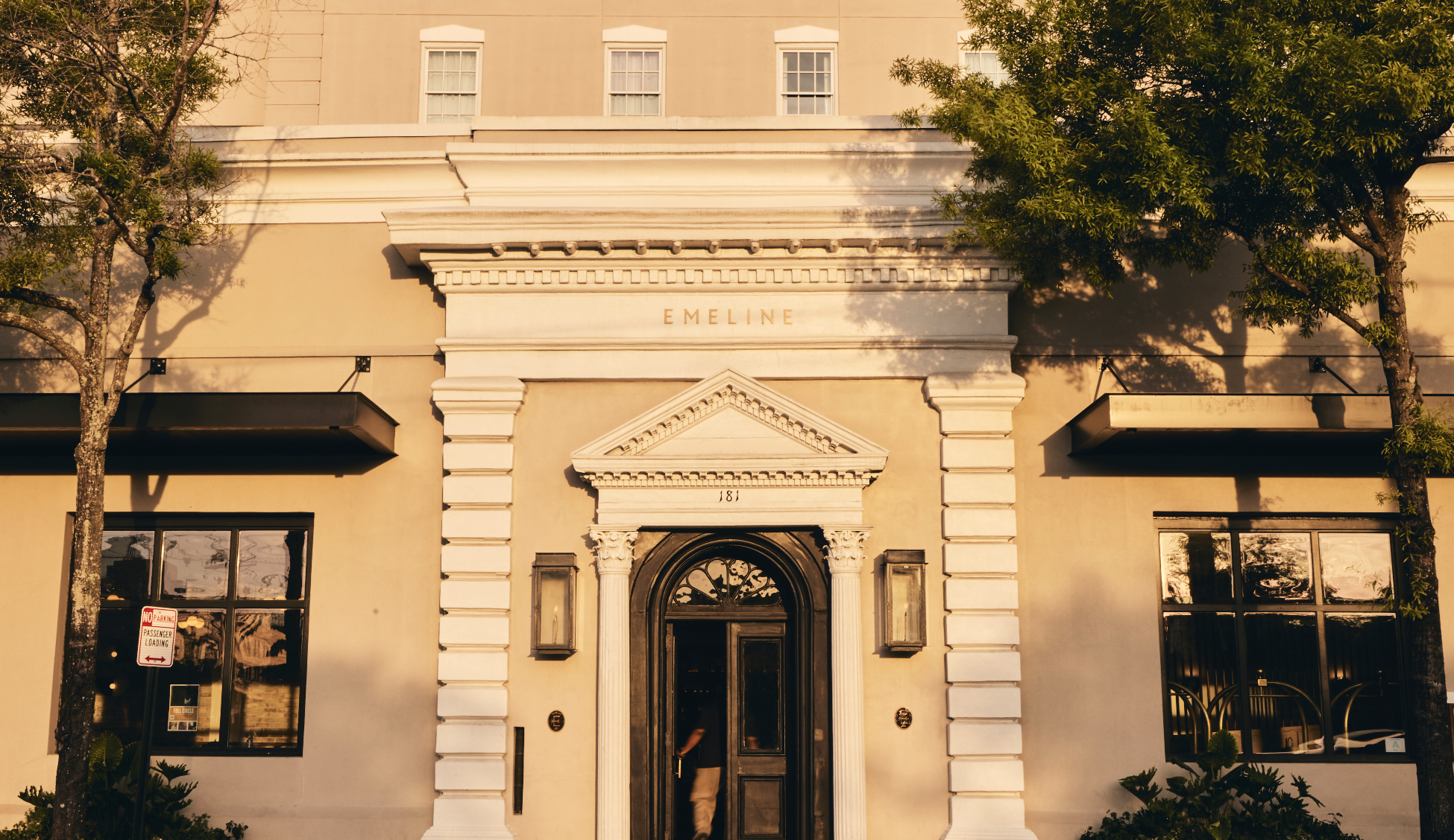Facade of a historic building with the name 'Emeline' and the number 181 above the door, flanked by trees and windows.