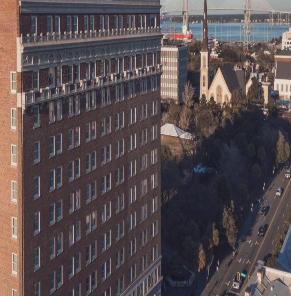 A city street with tall buildings, trees, and cars, overlooking a body of water with a bridge in the background.