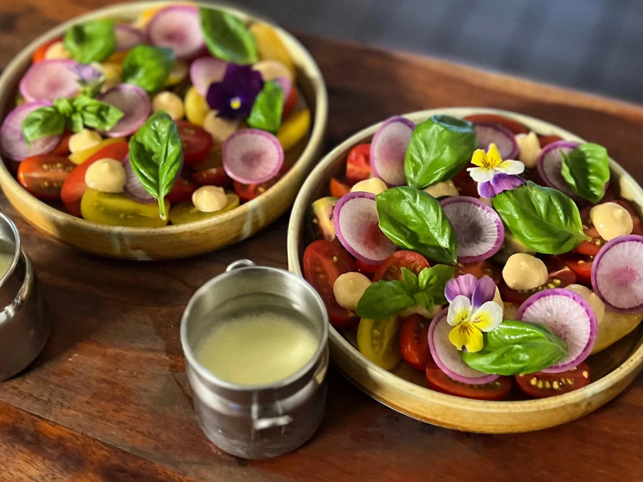 Two bowls of colorful vegetable salad with cherry tomatoes, radish slices, basil leaves, and edible flowers on a wooden table. Shows an option for full service catering for weddings, graduations, special events, birthdays