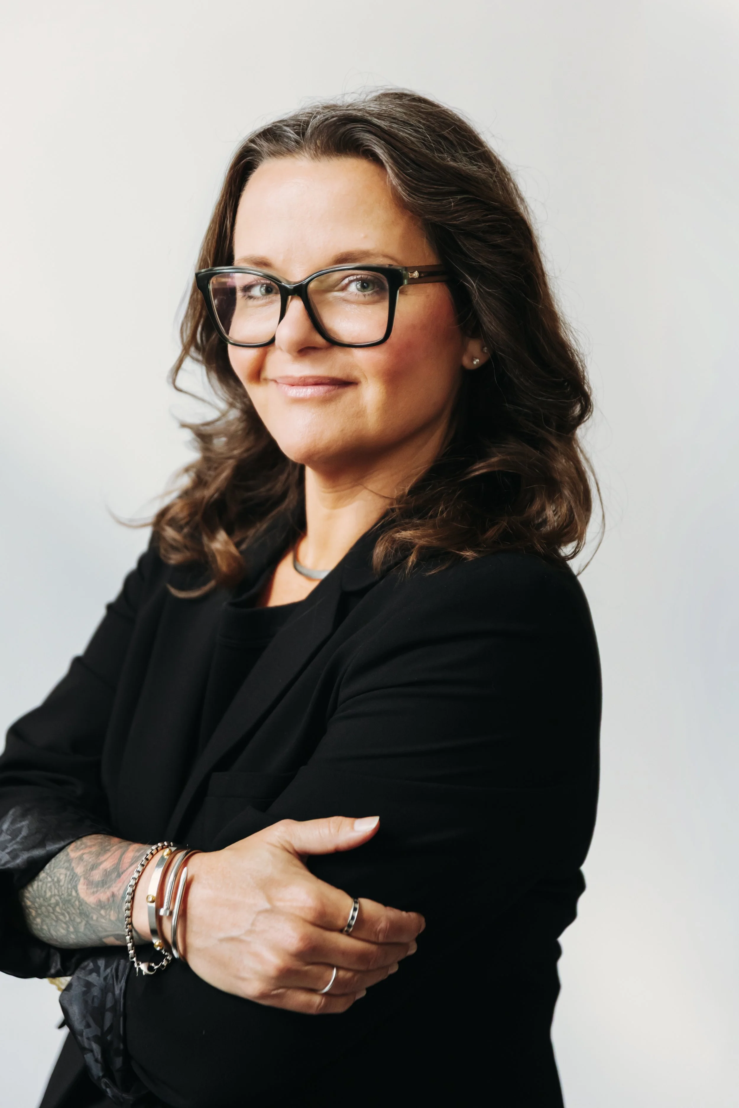Connie Woolsey in a black blazer, arms crossed, standing against a plain white background.