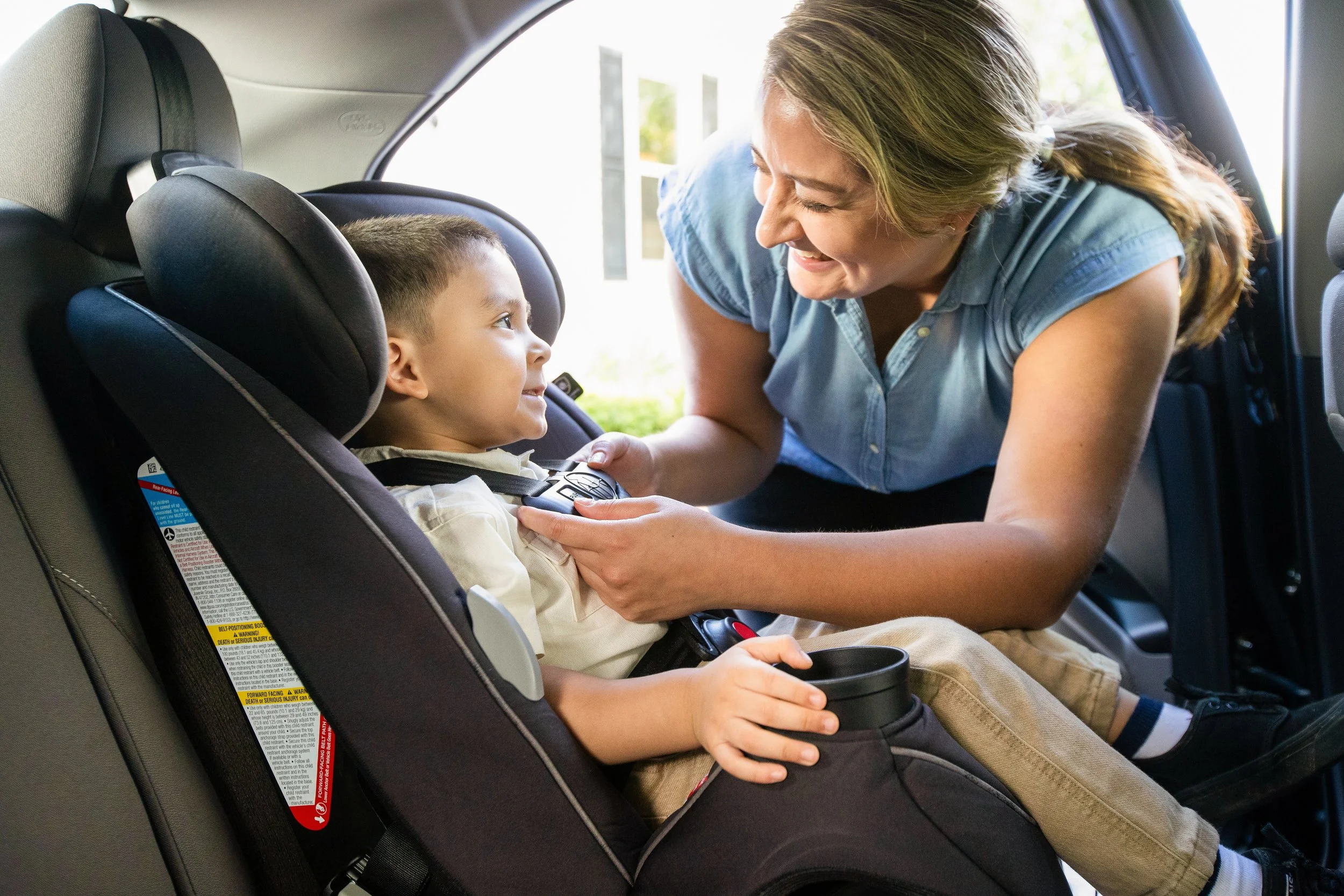 A Grandmother helping a child buckle his forward facing car seat
