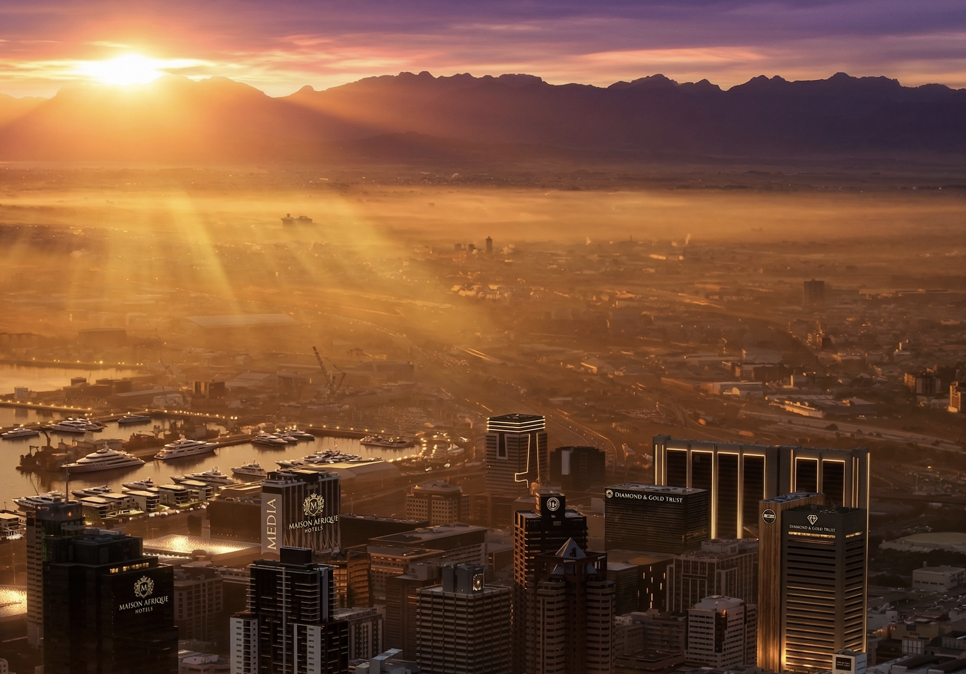 A city skyline at sunrise with high-rise buildings, yachts in the harbor, and mountains in the distance.