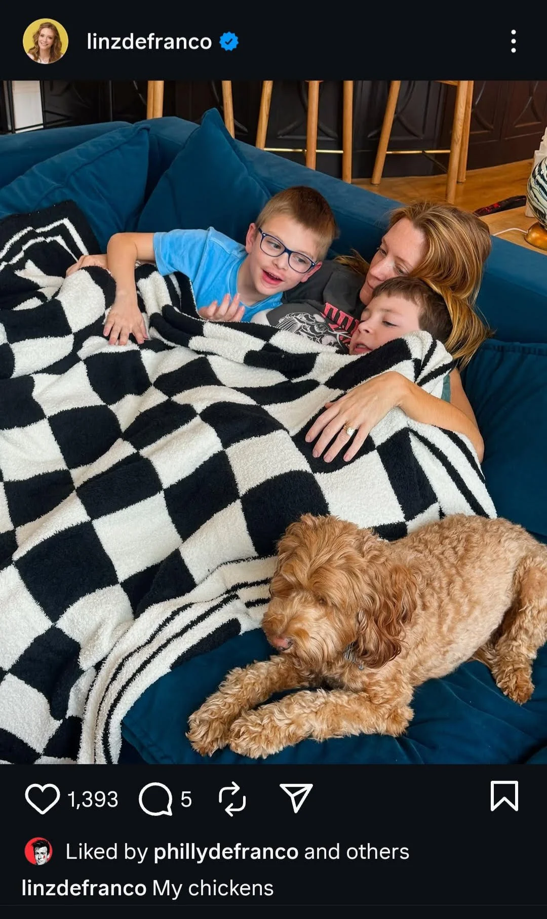 A woman and two children lying on a blue couch covered with a black and white checkered blanket, with a brown curly-haired dog lying nearby. The caption reads, 'My chickens.'