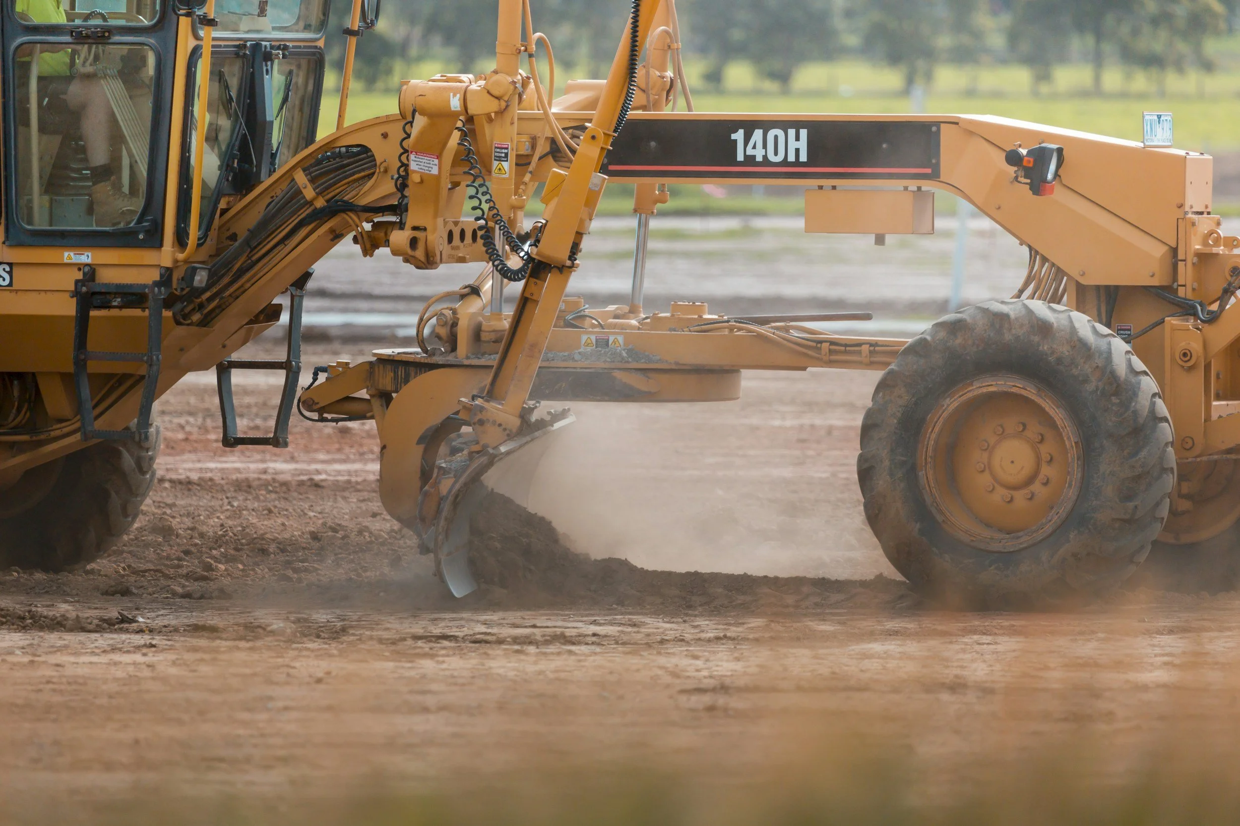A yellow bulldozer smoothing and leveling a dirt surface on a construction site with a green landscape in the background.